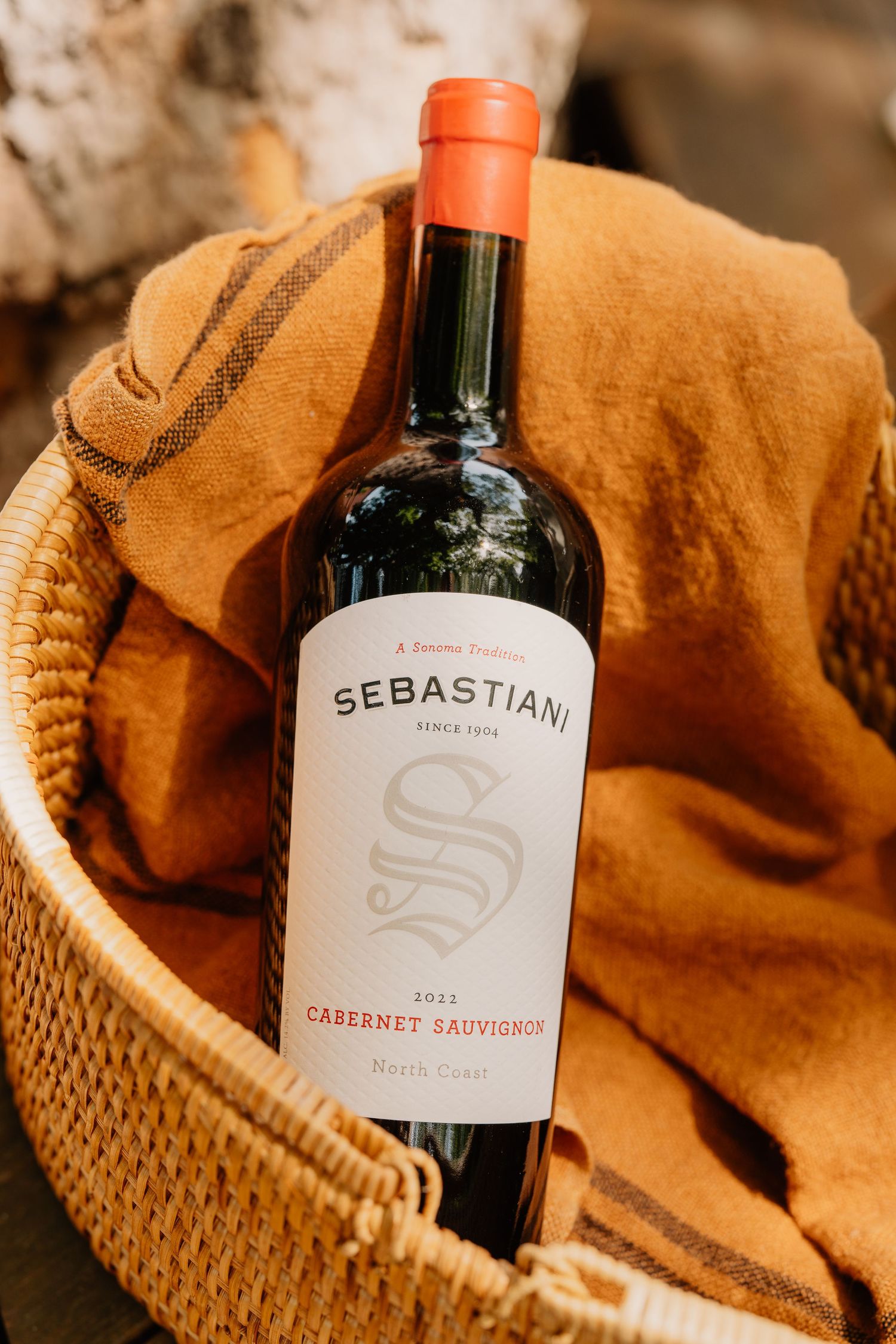 Sebastiani Cabernet Sauvignon wine bottle in a woven basket with an orange blanket.