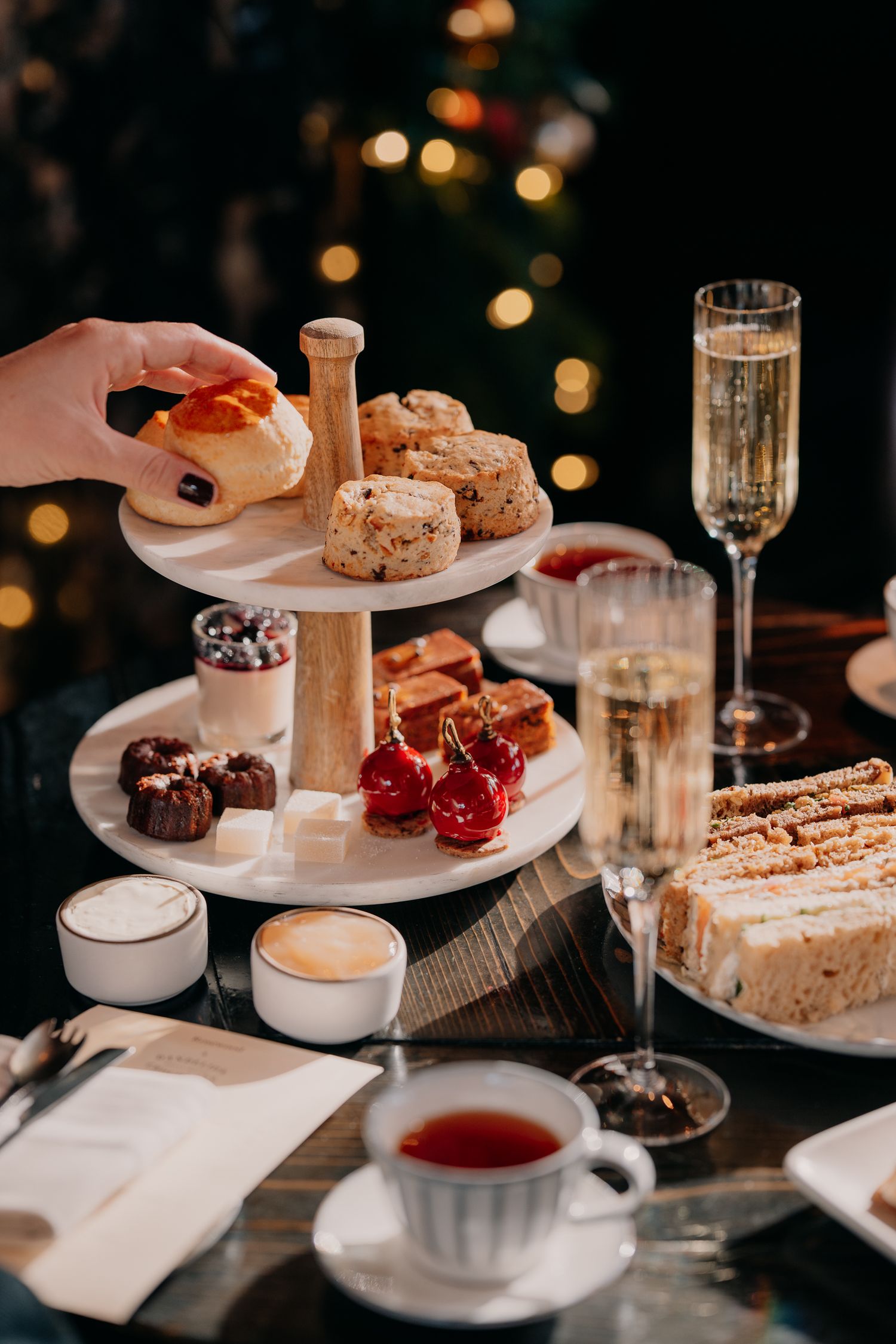 Elegant afternoon tea setting with pastries, cakes, and hot beverages served on white plates against a dark background.