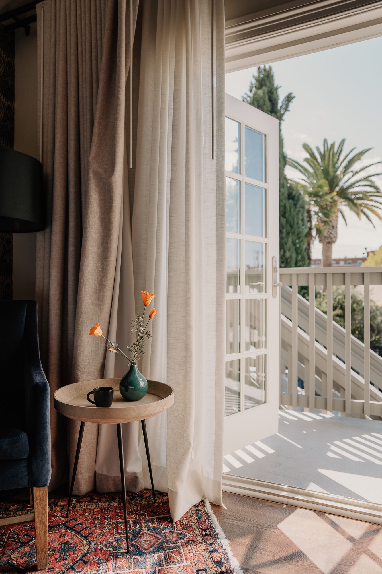 Sunlit room with floor-to-ceiling windows, flowing curtains, and oriental rug creating a cozy seating nook.