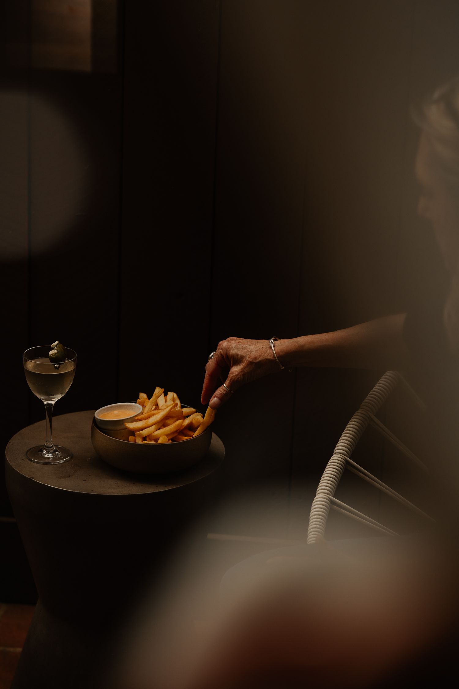 Elegant restaurant dining scene with wine glasses, french fries, and plates in moody, dark lighting.