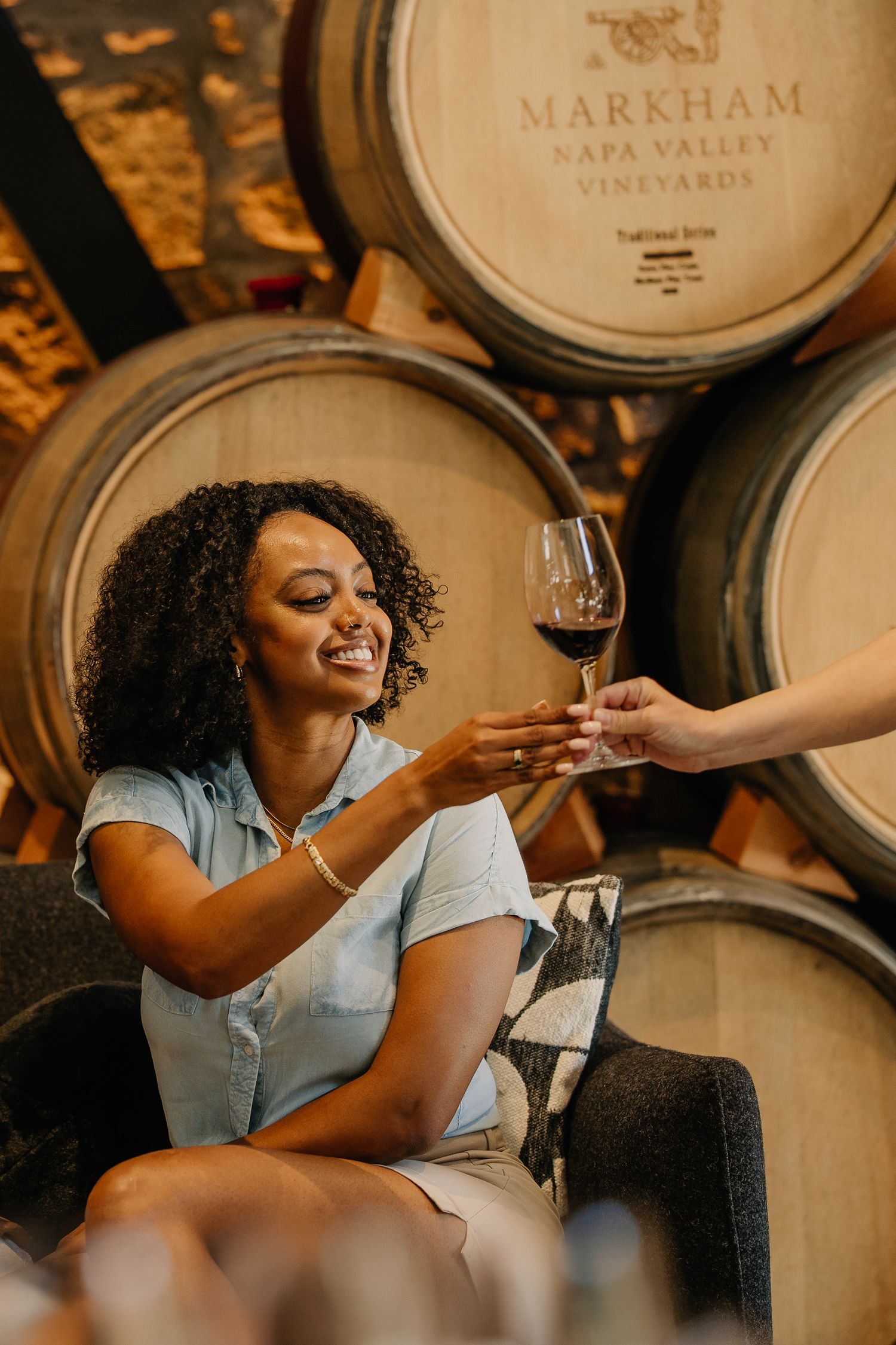 Woman smiling receiving a glass of red wine in Markham Napa Valley Vineyards barrel room.