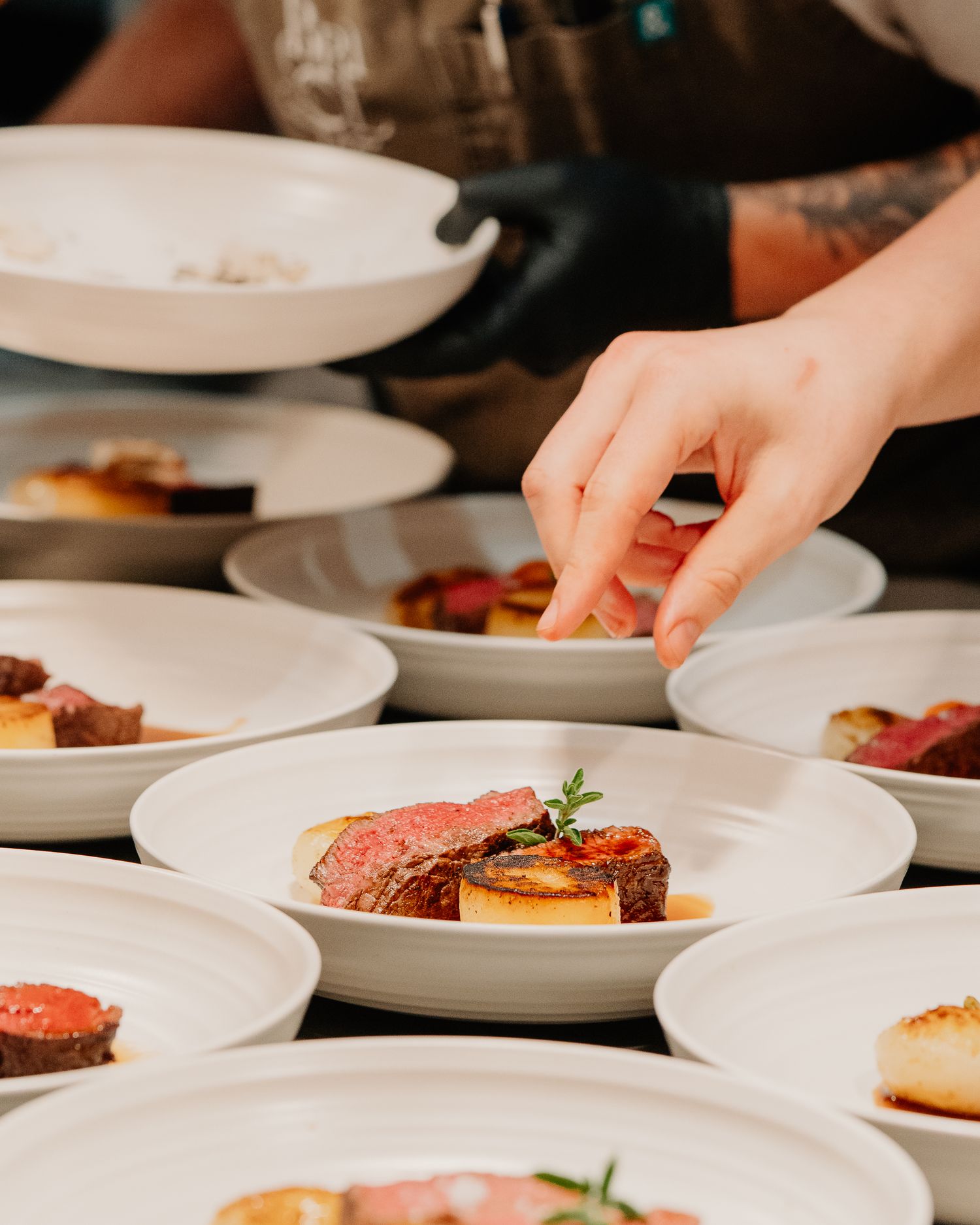 A plating chef's hand arranges sliced meat dishes with garnish on white plates for an elegant dining service.