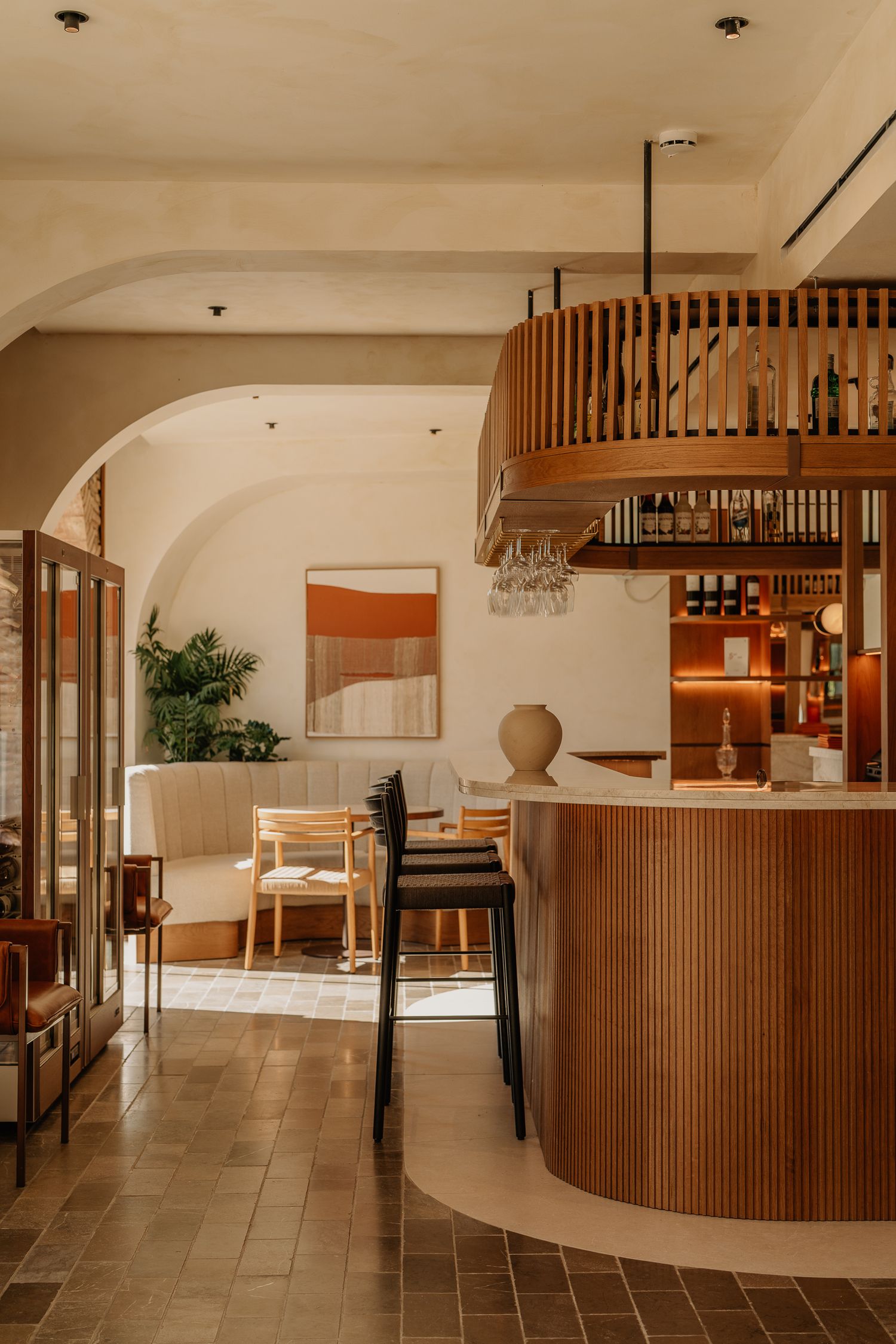 Modern restaurant interior with curved wooden bar, warm lighting, and minimalist decor featuring arched ceilings.