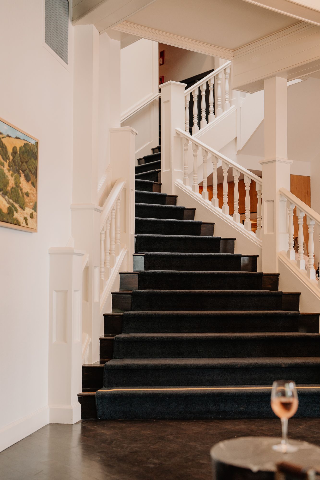 An elegant staircase with black steps and white wooden railings ascends against a white wall with artwork.