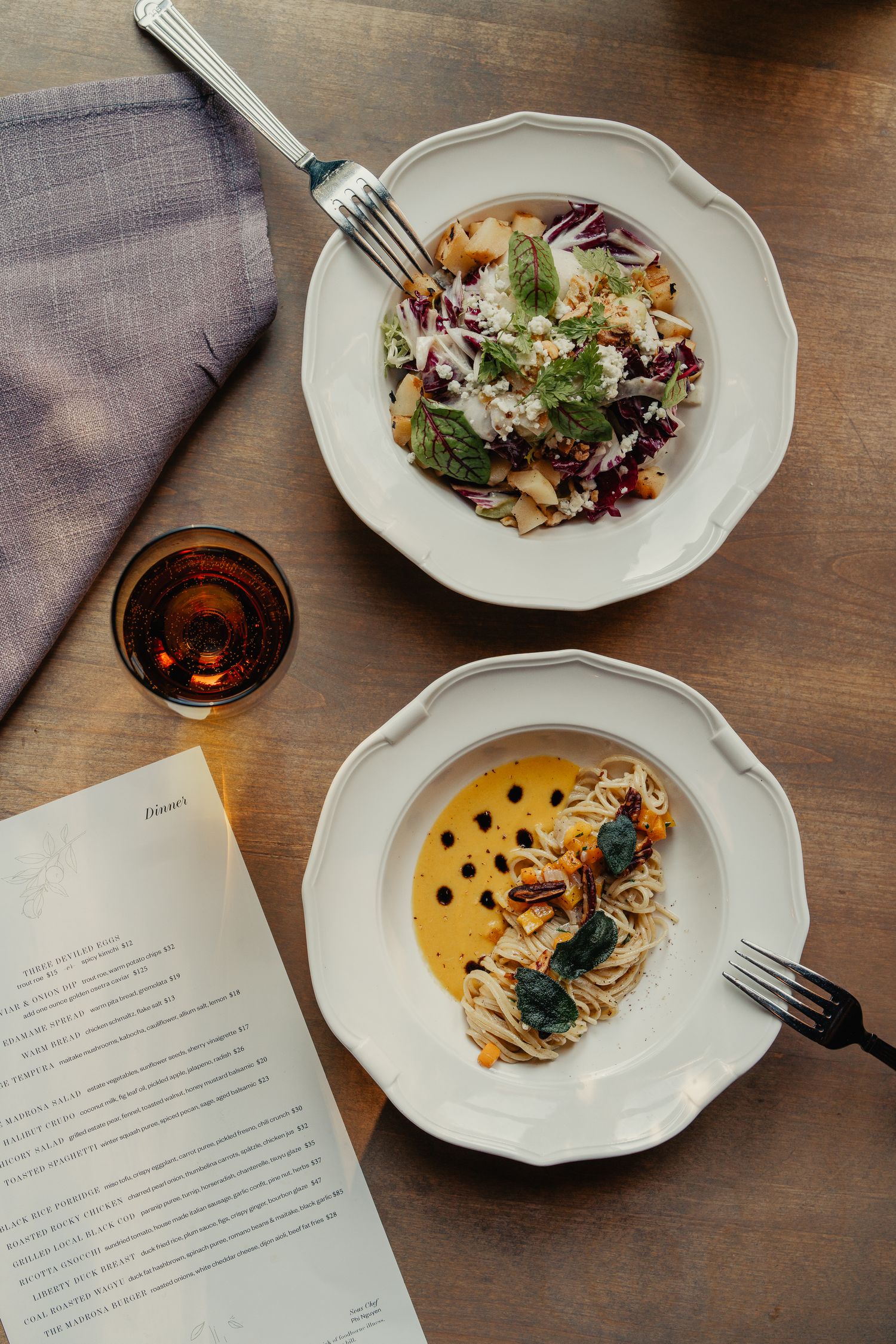 Multiple gourmet dishes served on white plates alongside a menu on a wooden table.