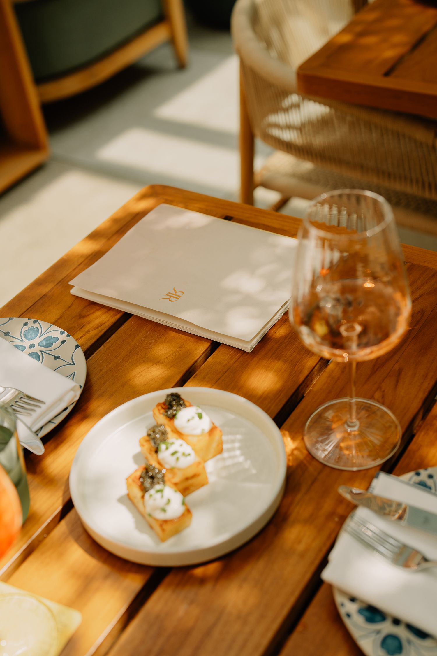 Wooden dining table set with small desserts on white plates and wine glasses in natural lighting.