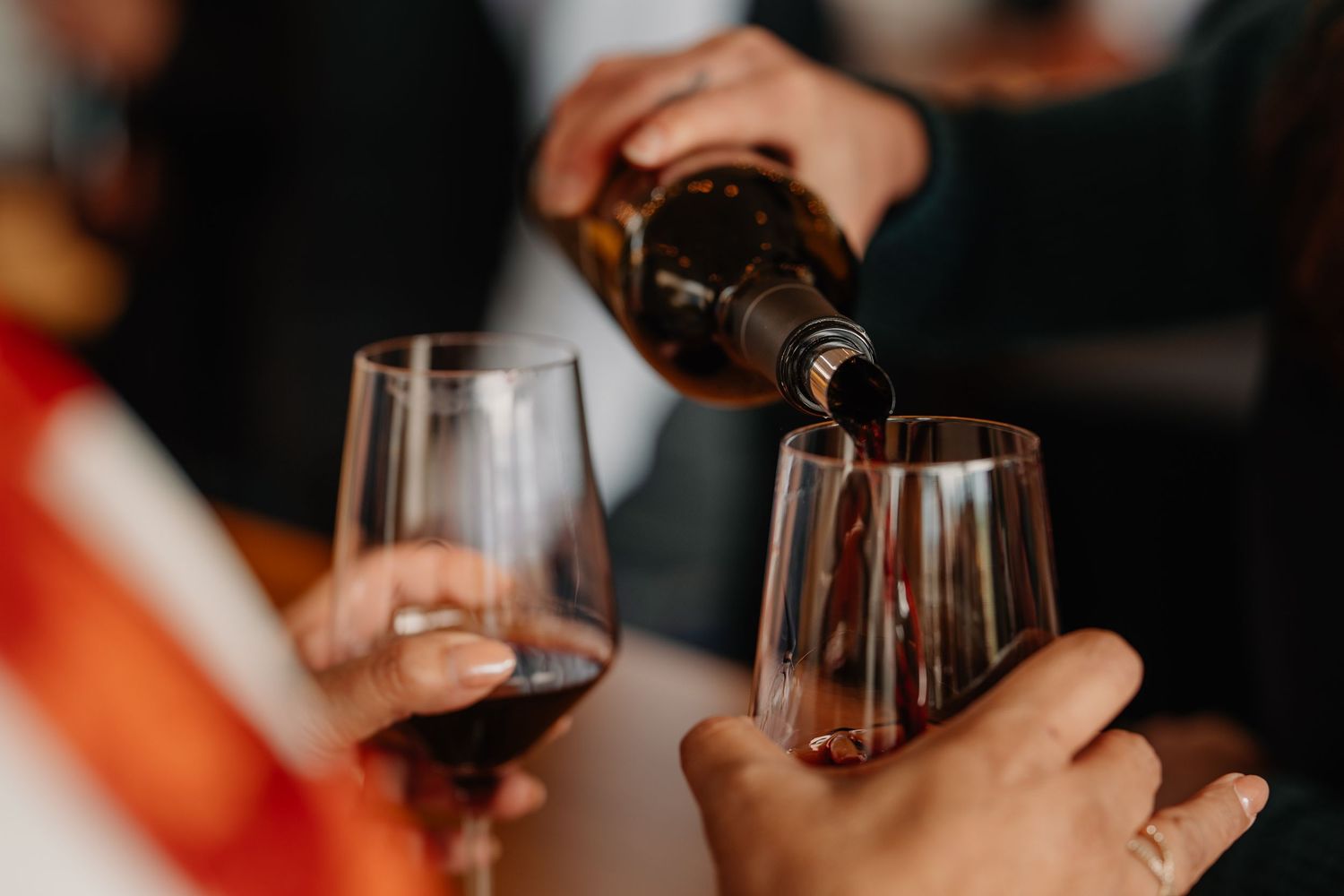 Someone pouring red wine into glasses at a social gathering event.