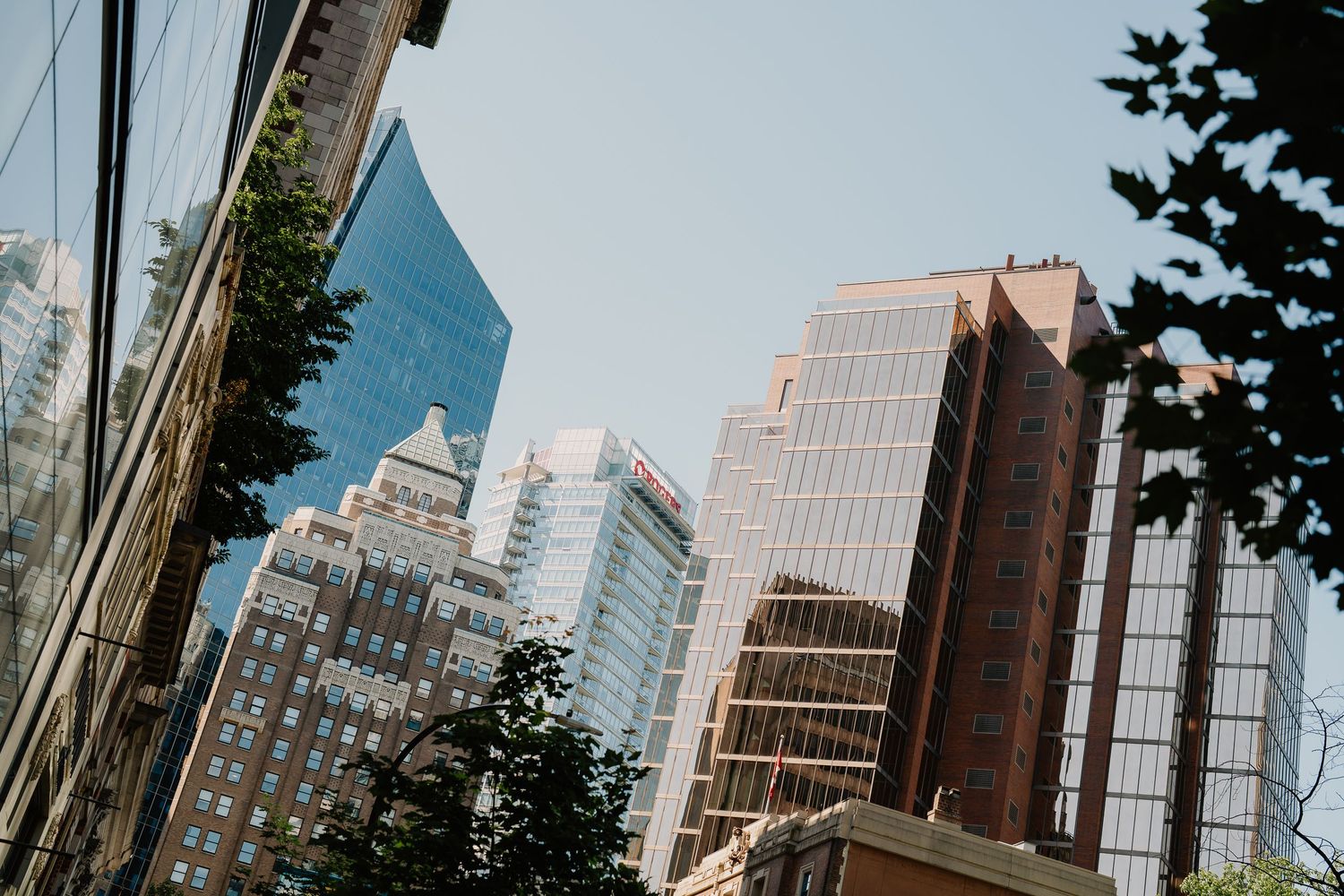 Modern office buildings and skyscrapers with glass facades tower against a bright sky in a bustling downtown city center.