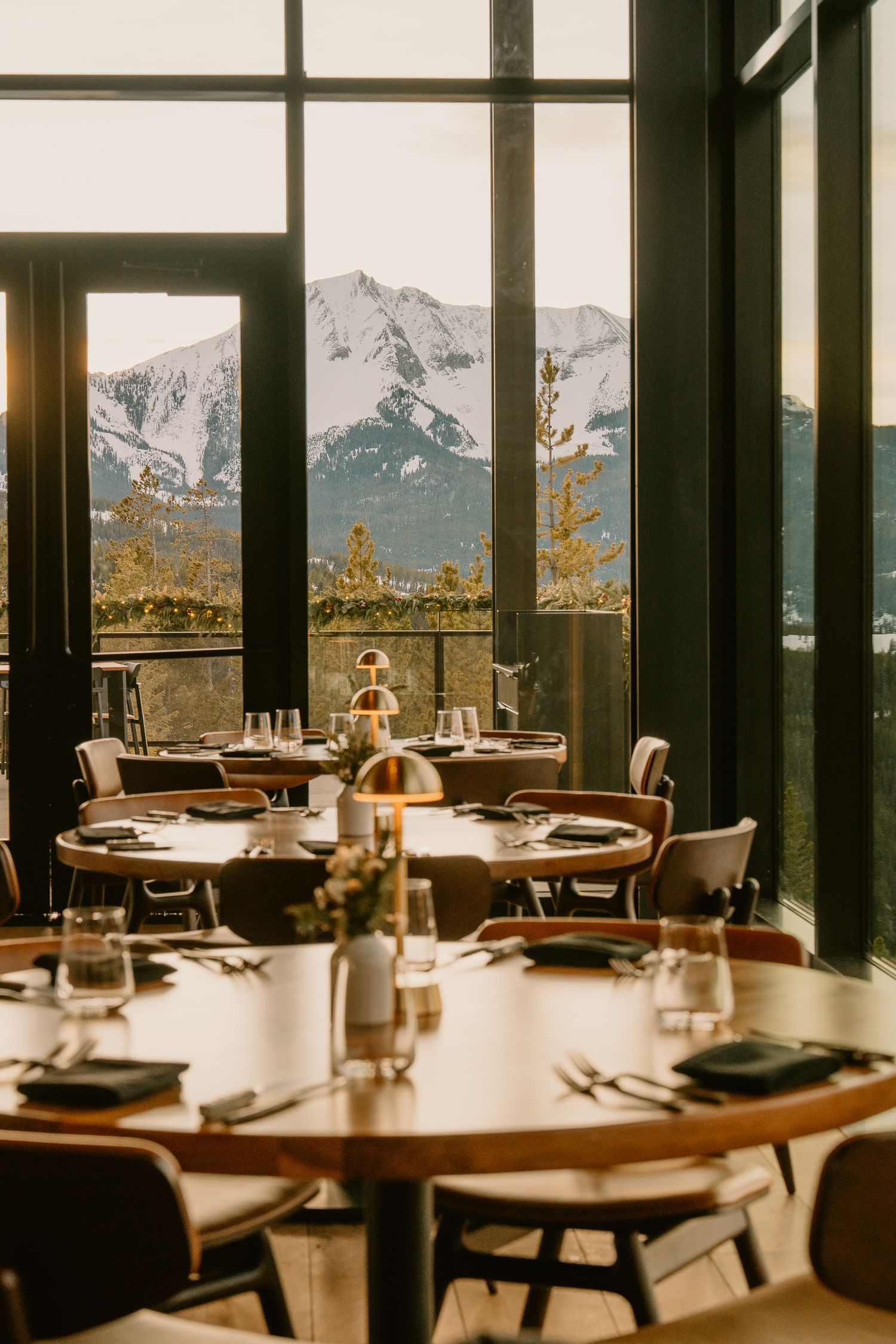 Upscale restaurant dining room with panoramic mountain views through large windows and elegant table settings.