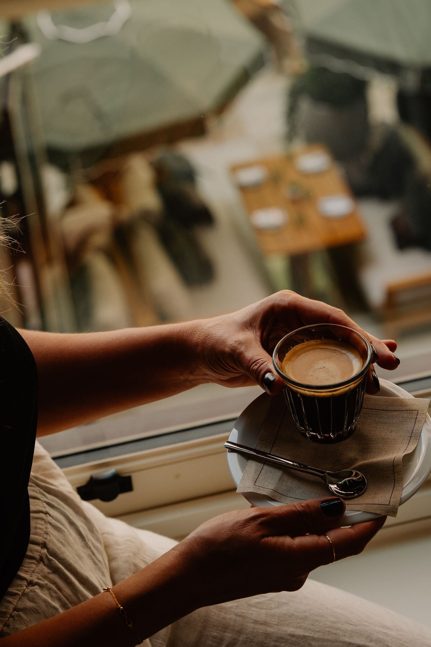 Hands holding a steaming cup of coffee on a wooden table with books in warm natural lighting.