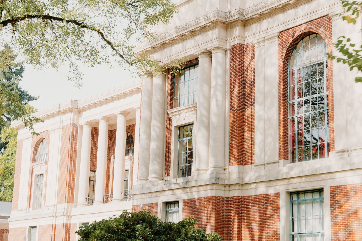 Historic stone building exterior with arched windows and columns casting shadows in warm sunlight.