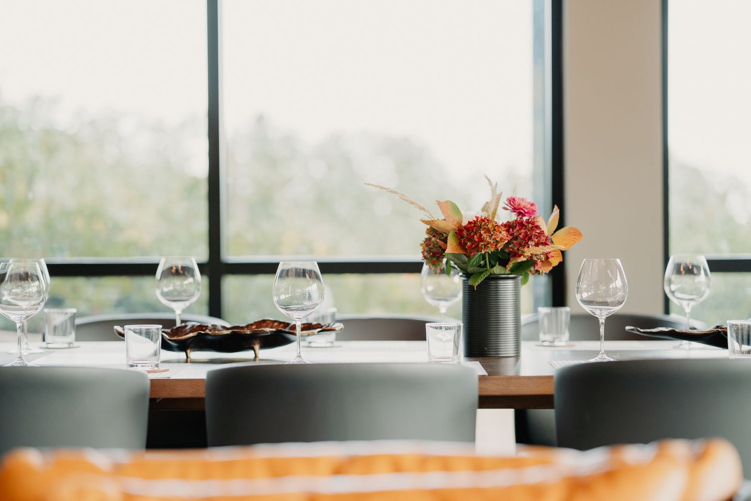 Elegant restaurant table setting with wine glasses and floral centerpiece near bright window.