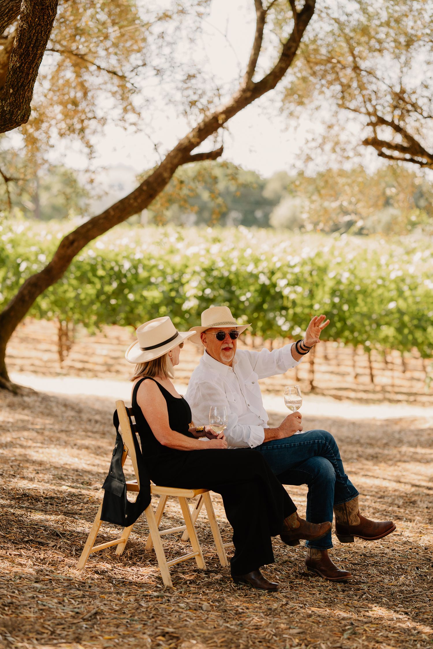 Two people enjoying wine while sitting in wooden chairs at a vineyard on a sunny autumn day in California.