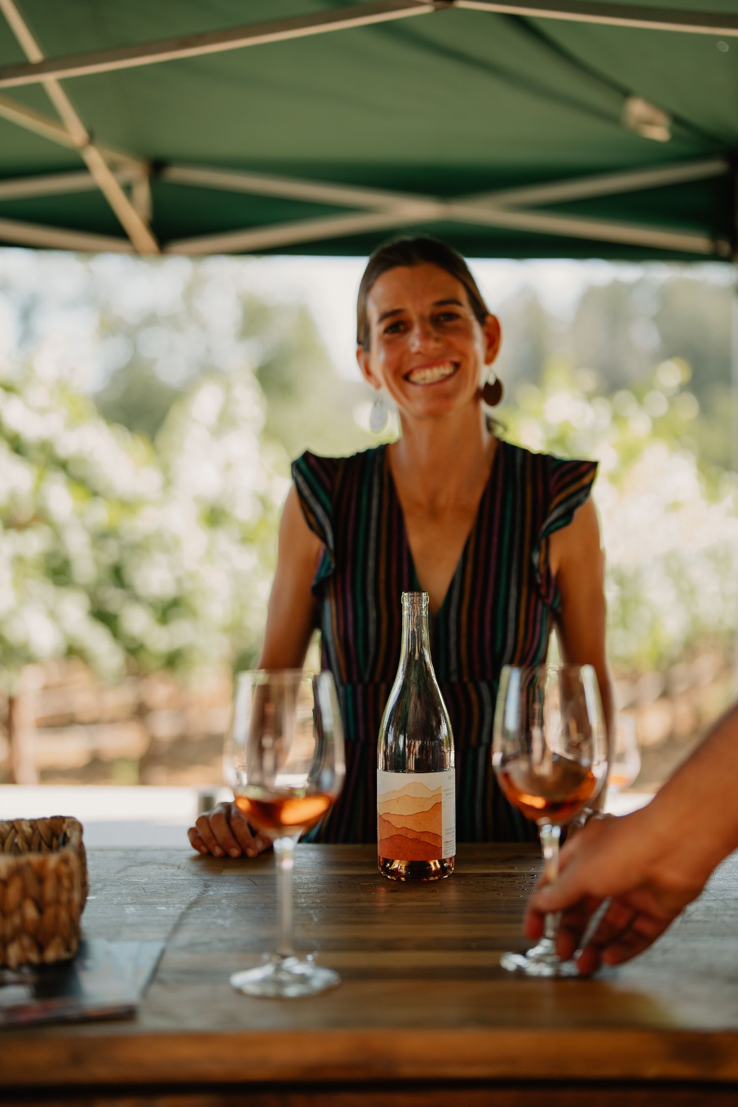 Wine glasses and cocktails sit on a wooden table during an outdoor tasting event.