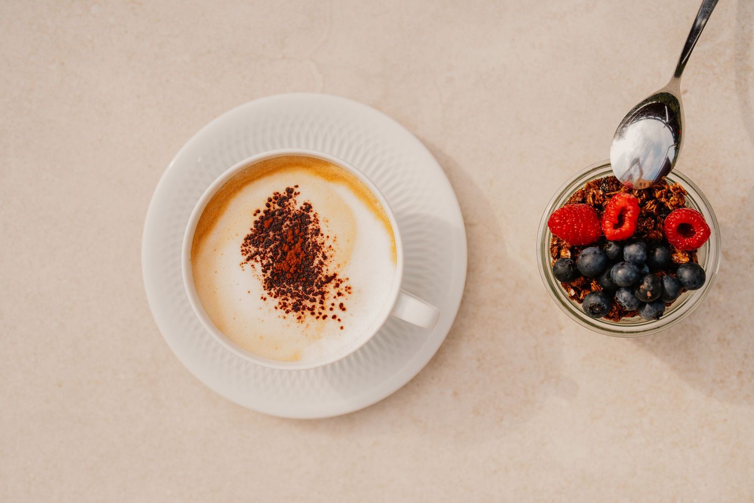 Overhead view of coffee cups and fresh berries arranged on a light beige surface.