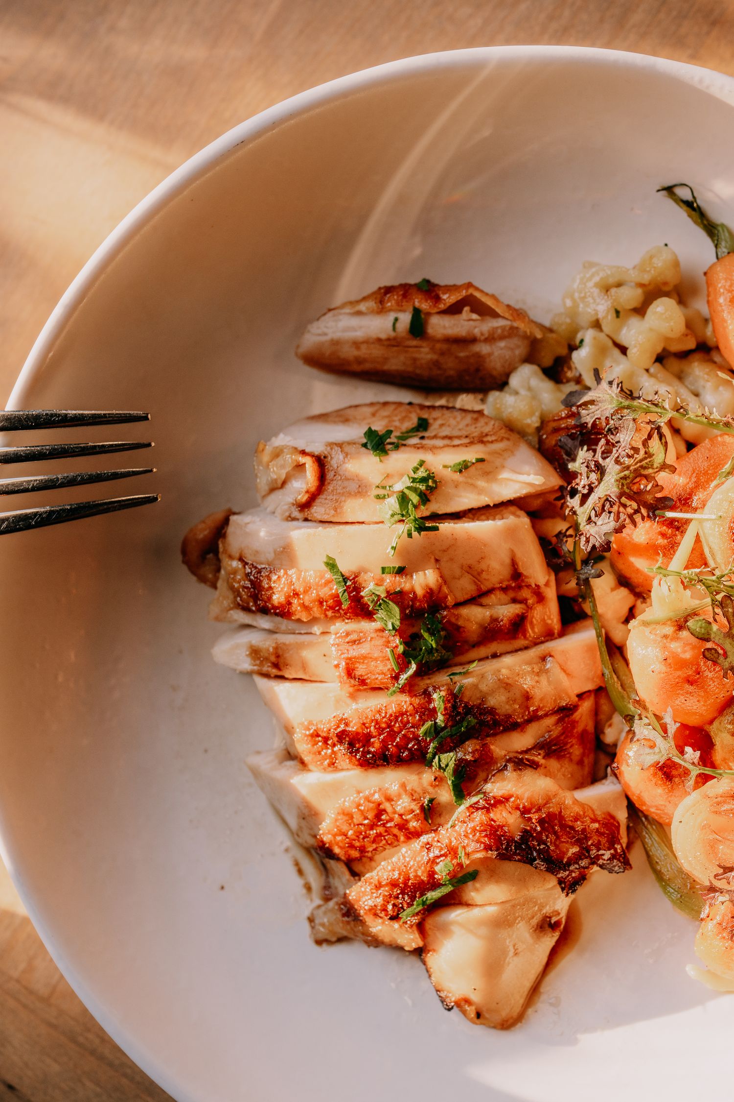 Grilled chicken breast sliced on a white plate garnished with fresh herbs and seasonings.