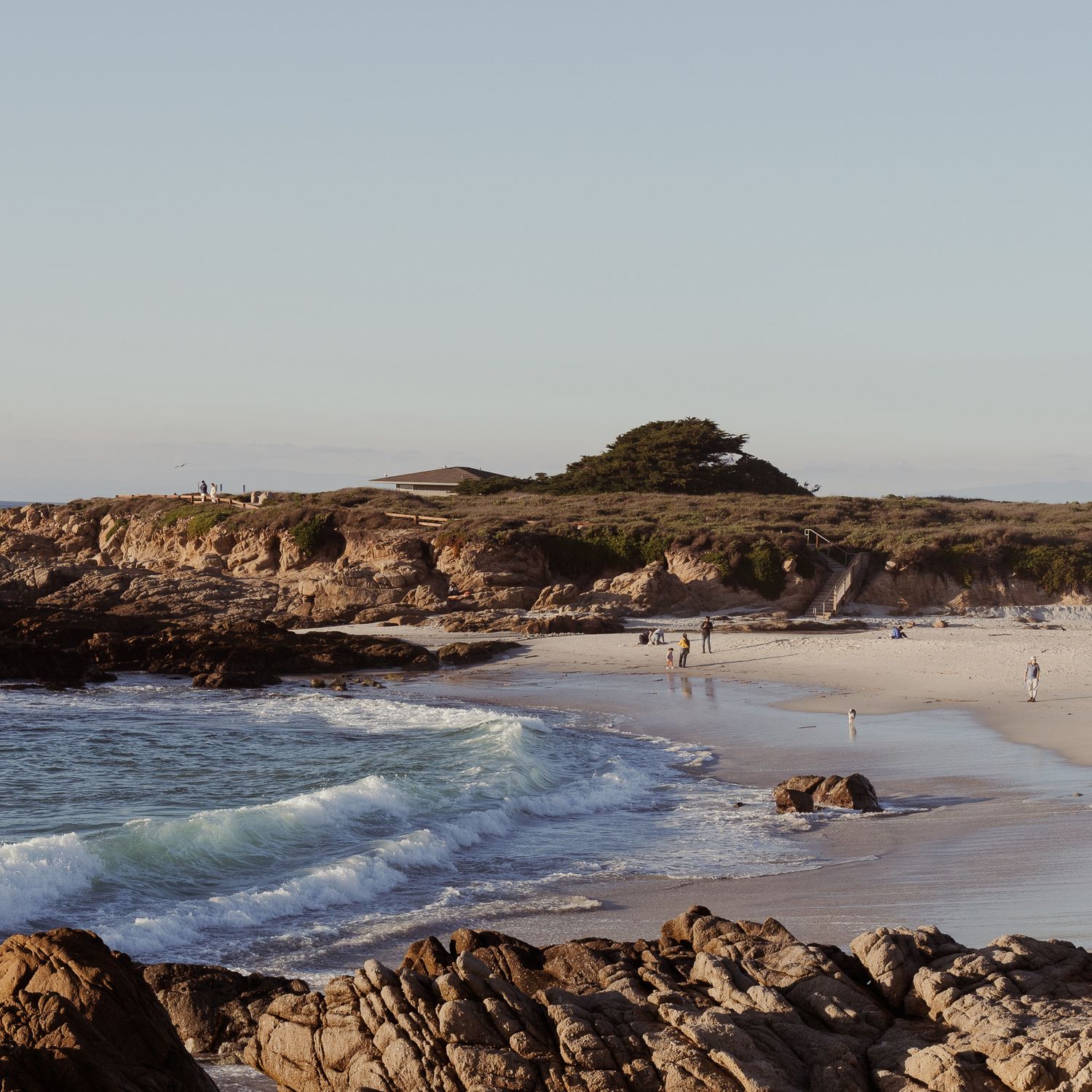 Panoramic view of a rocky coastal beach with crashing waves and sandy shores stretching along the rugged coastline.