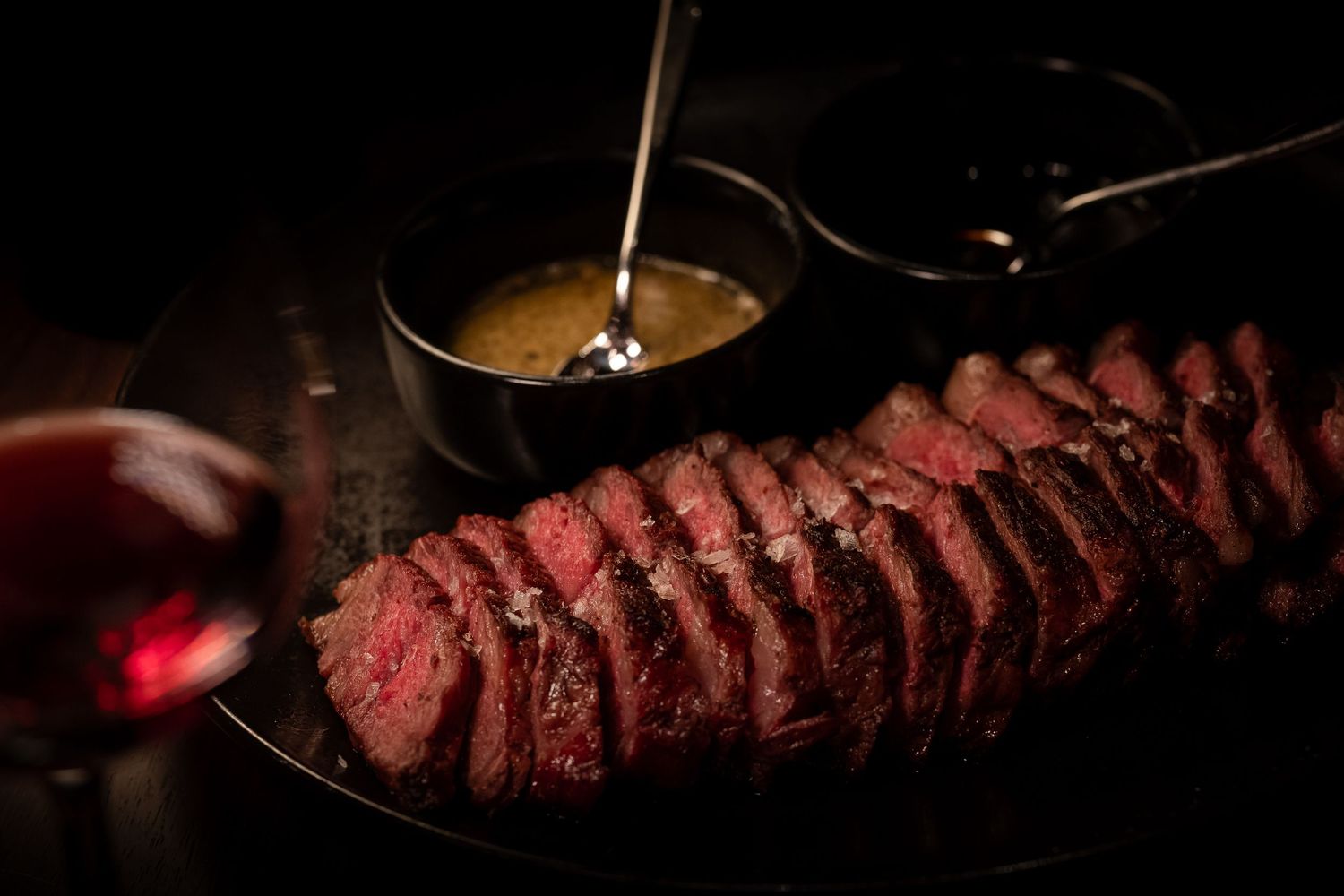 Sliced medium-rare steak arranged in rows on a dark surface with dramatic lighting.