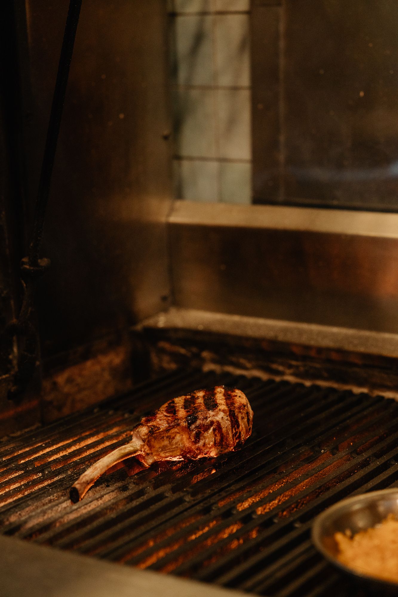 A juicy tomahawk steak with grill marks cooking on a commercial grill in a restaurant kitchen.