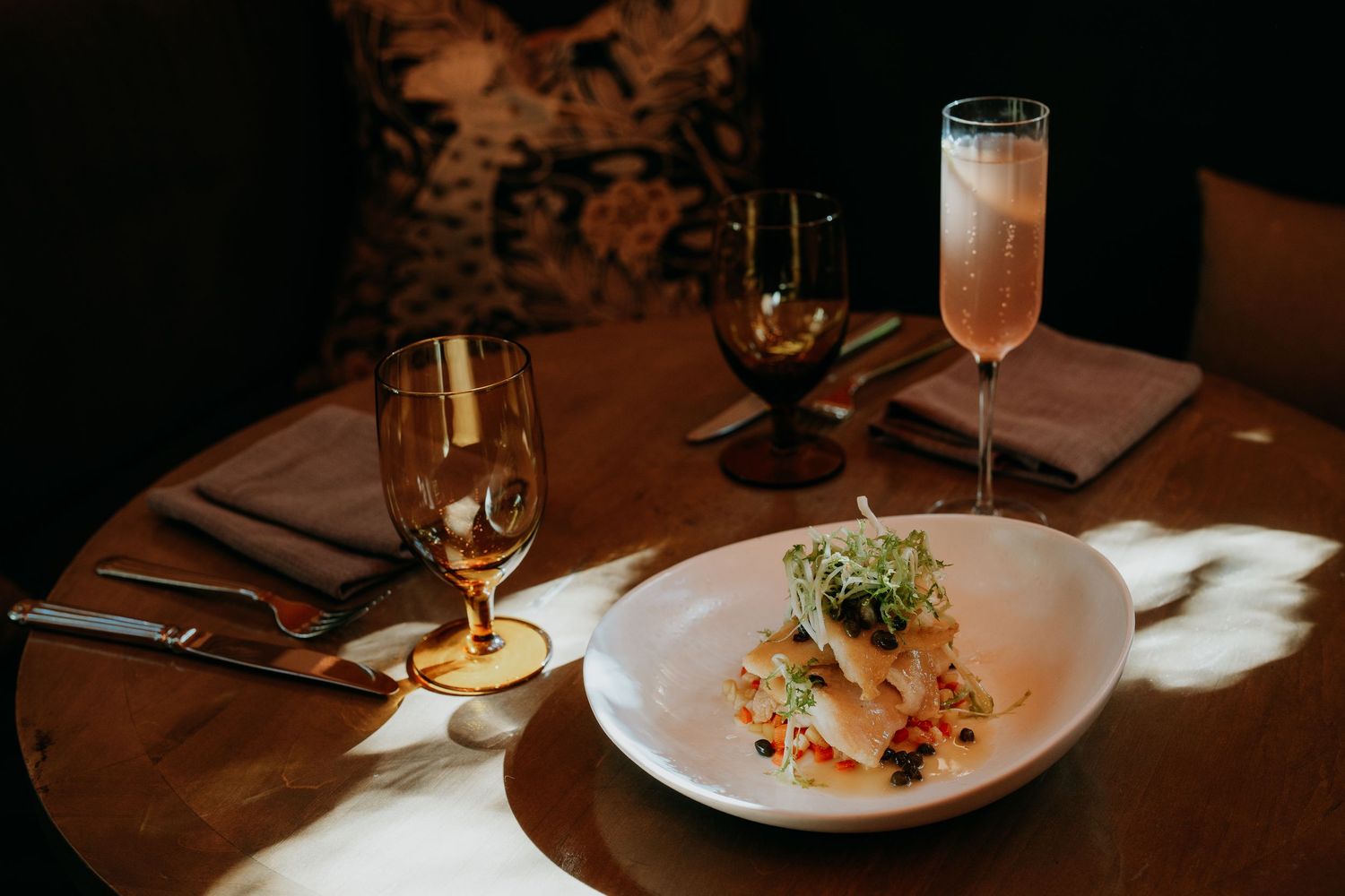 Restaurant table setting with wine glasses and plates in warm ambient lighting.