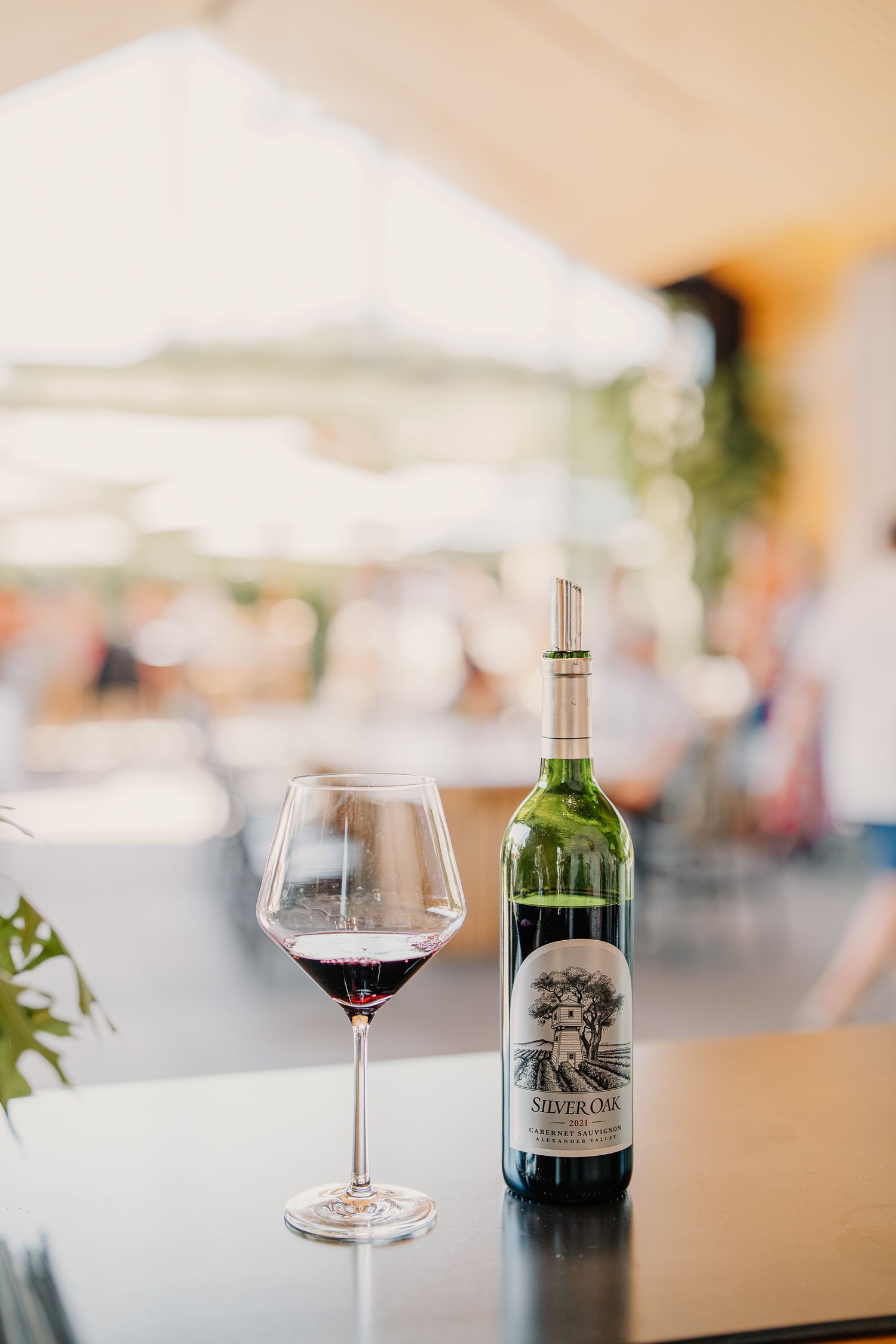 Silver Oak Cabernet Sauvignon wine bottle beside a filled red wine glass on a table at an outdoor venue.