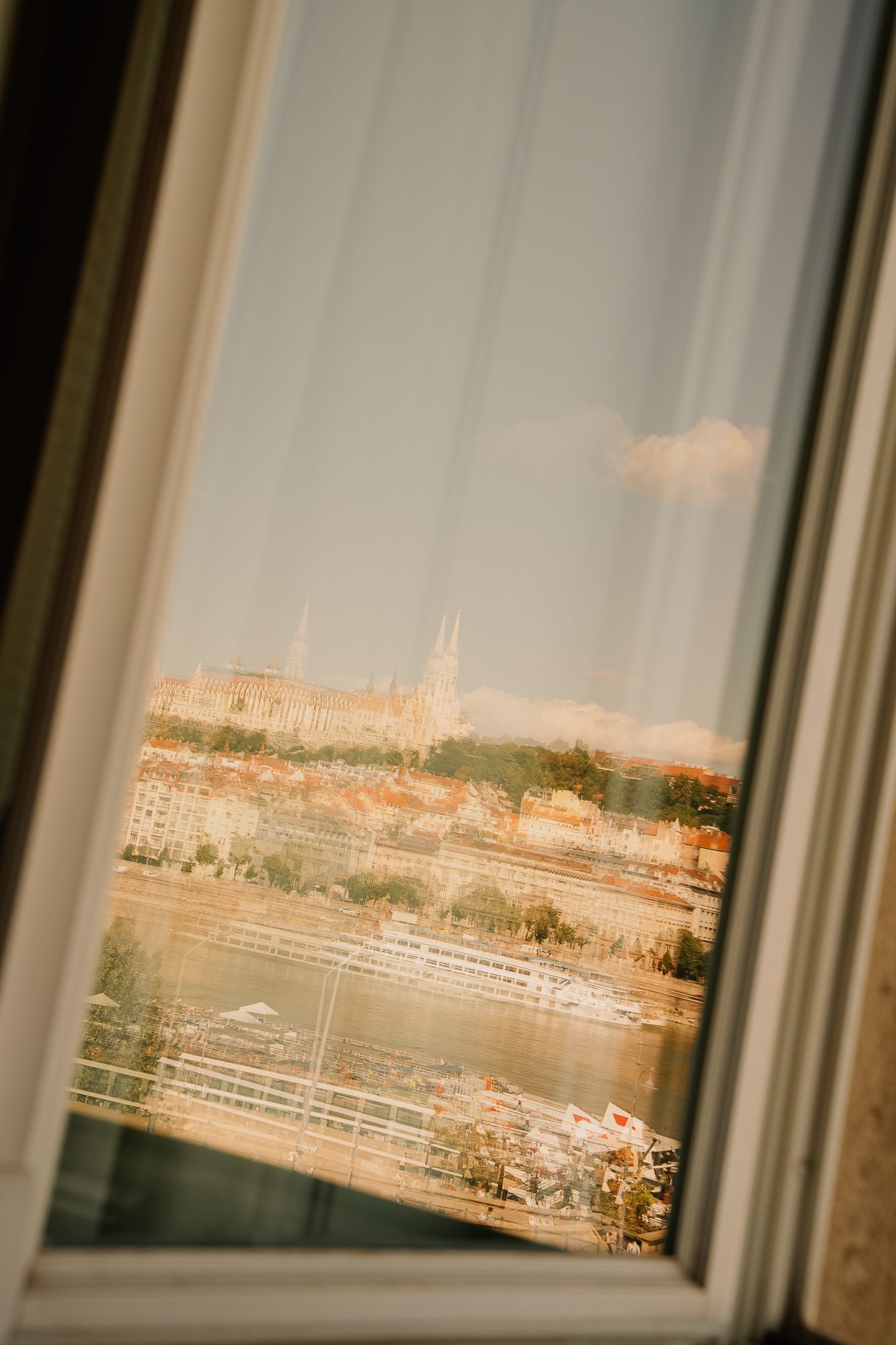 View through a window of Budapest cityscape with Matthias Church, Danube River, and cruise ships on a sunny day.