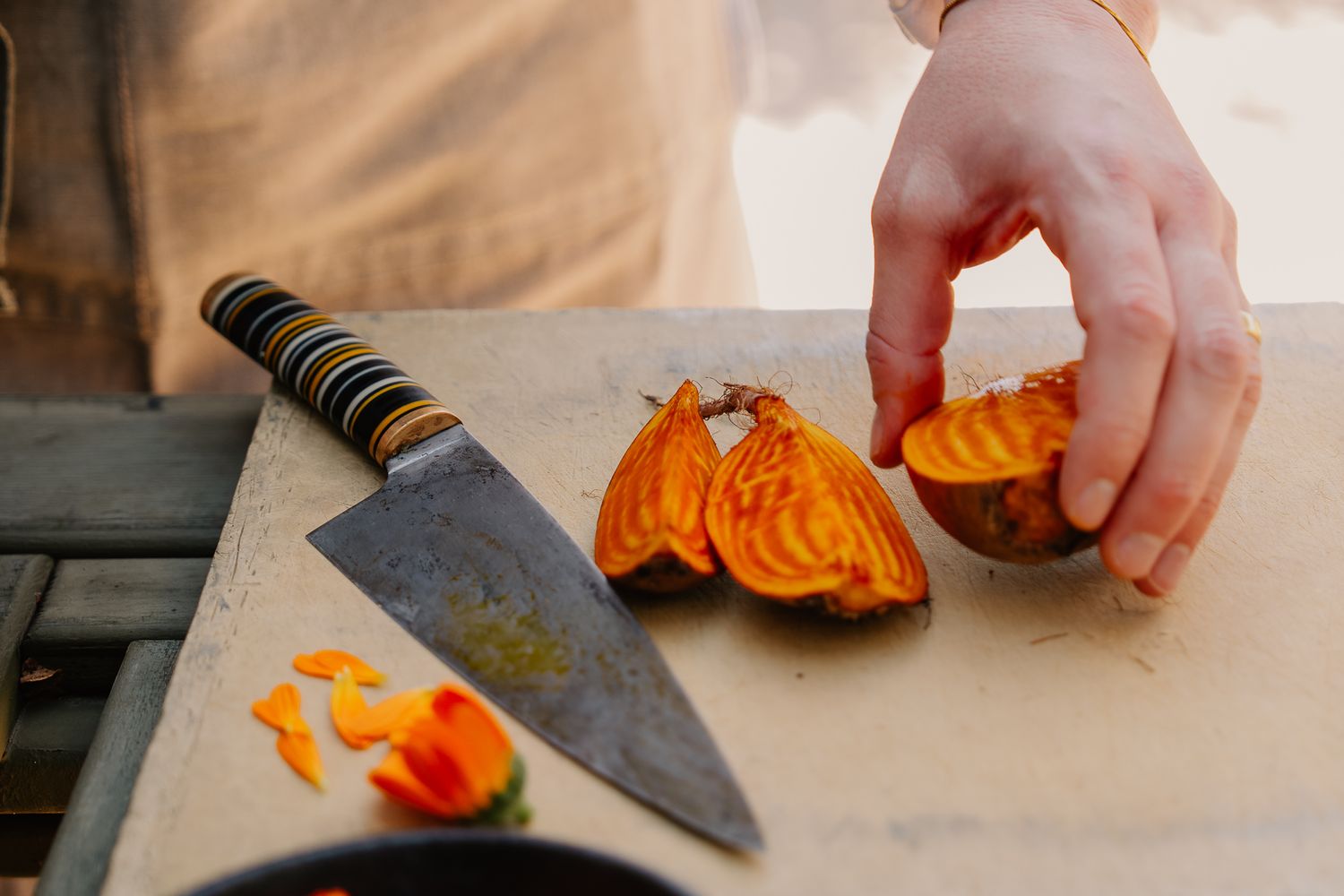 Hand slicing golden beet on wooden cutting board with chef knife, fresh vegetable preparation in kitchen.