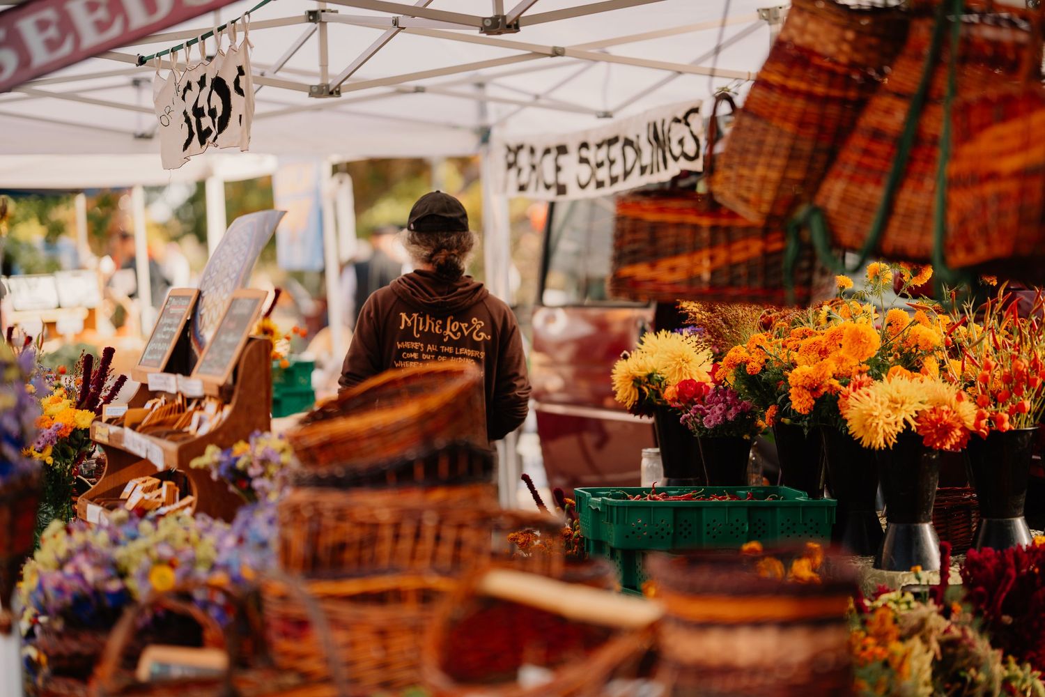 Colorful flower bouquets and woven baskets for sale at an outdoor farmers market vendor stall during a bright summer day.