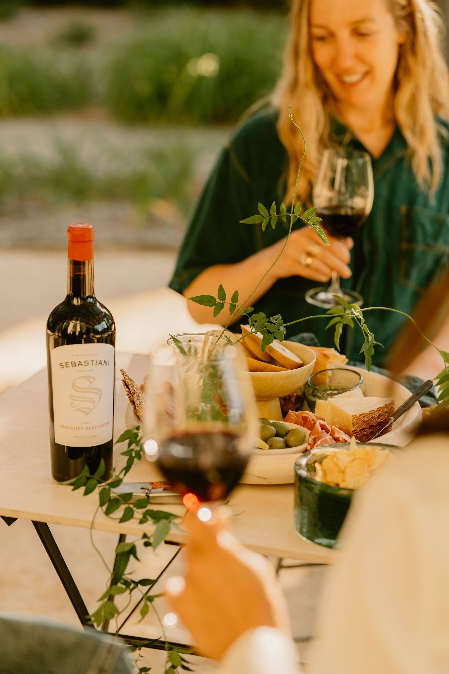 Woman smiling at outdoor dinner table with Sebastiani wine bottle, charcuterie board, and red wine glasses.
