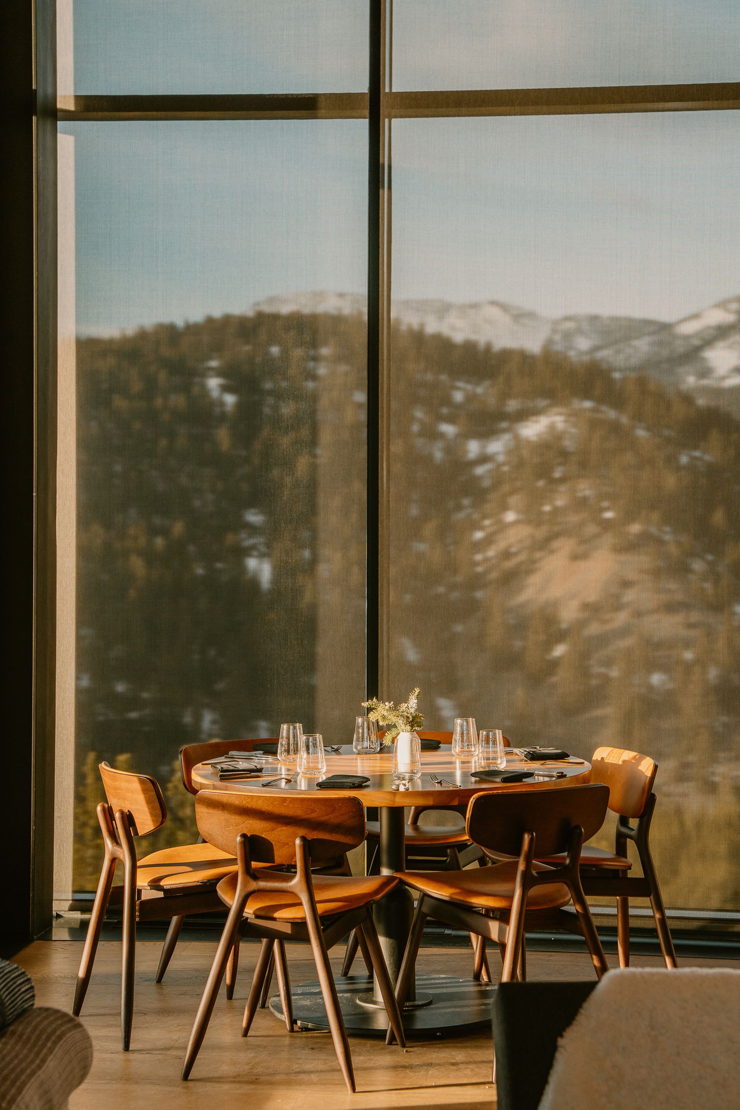 Mid-century modern dining setup with wooden chairs and mountain views through large windows.
