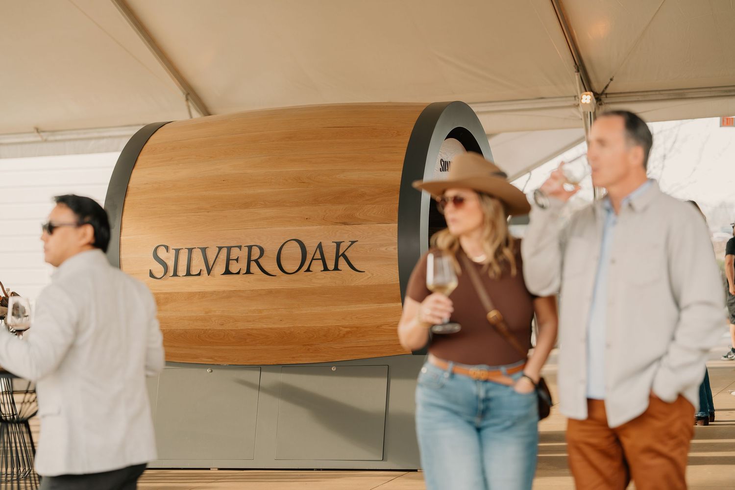 Guests enjoying wine near a large Silver Oak barrel display at an outdoor wine festival.