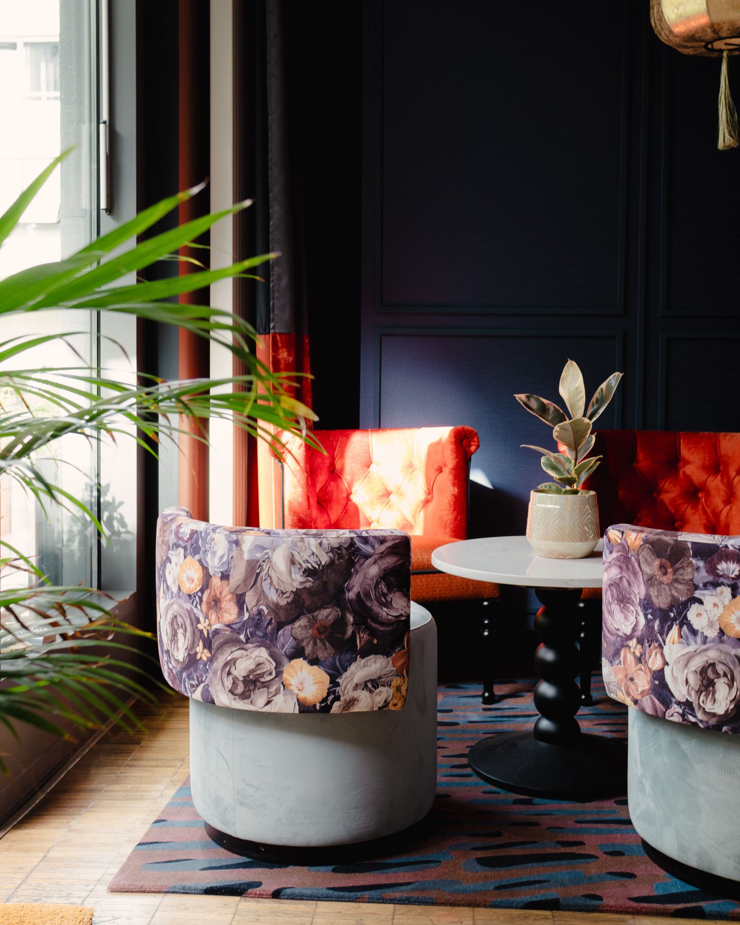 Modern interior decor with velvet ottomans featuring floral patterns and concrete bases against a dark wall with plants.