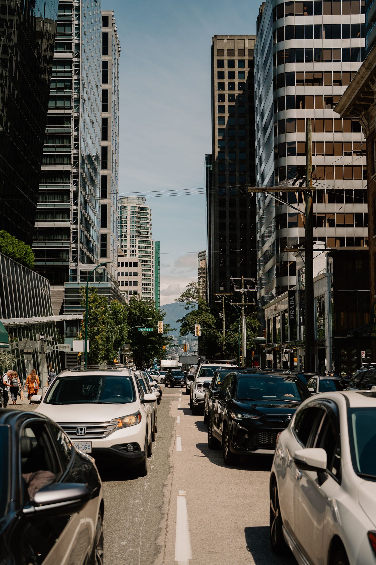 Downtown city street with high-rise buildings and parked cars leading to a mountain vista in the distance.