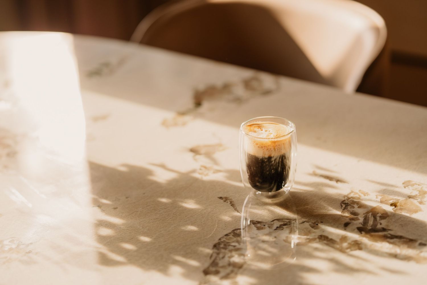A hand pours steamed milk into a coffee cup creating latte art on a white countertop in warm lighting.