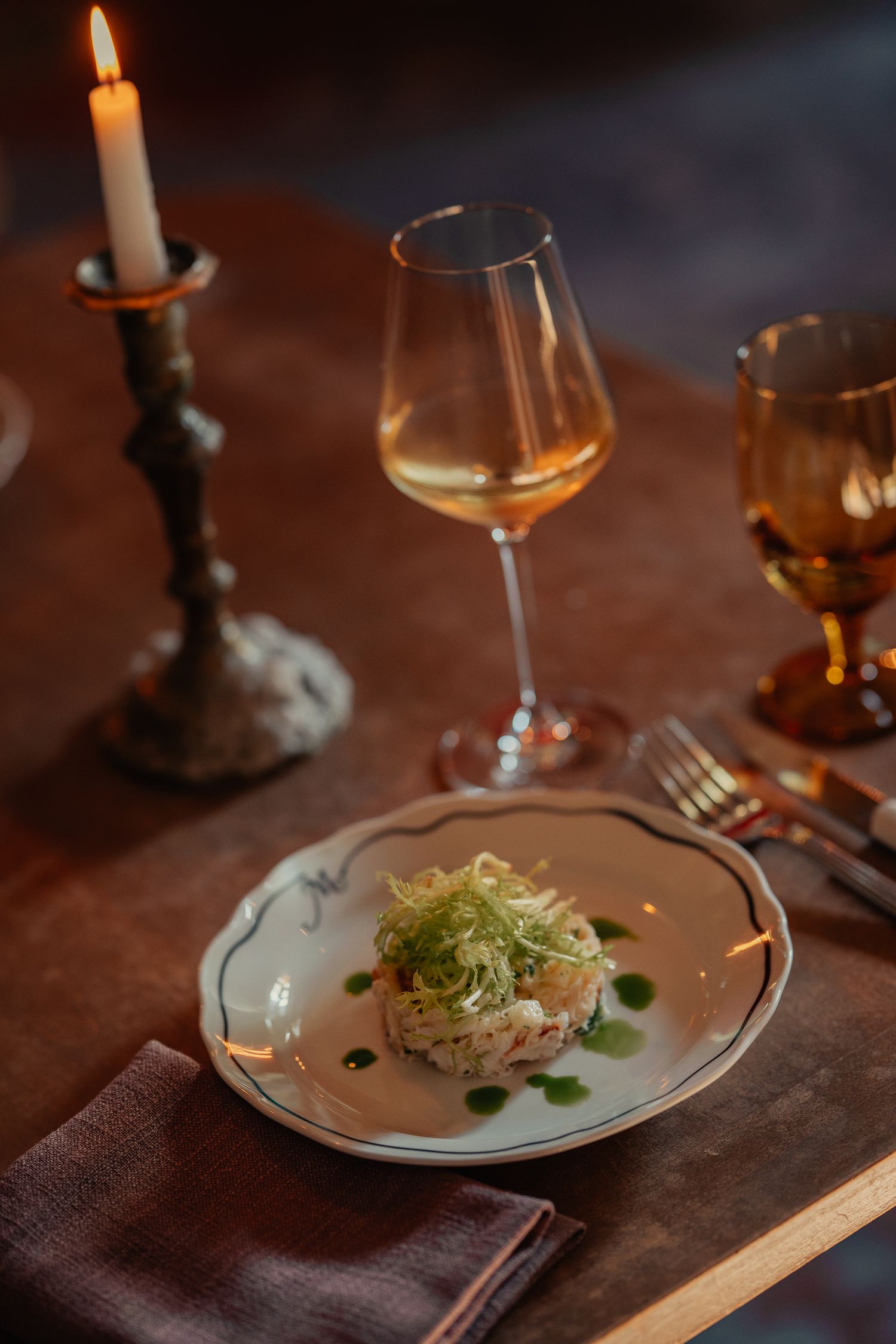 Elegant plated dish with microgreens and garnishes served on rustic table with candlelight and wine glasses.