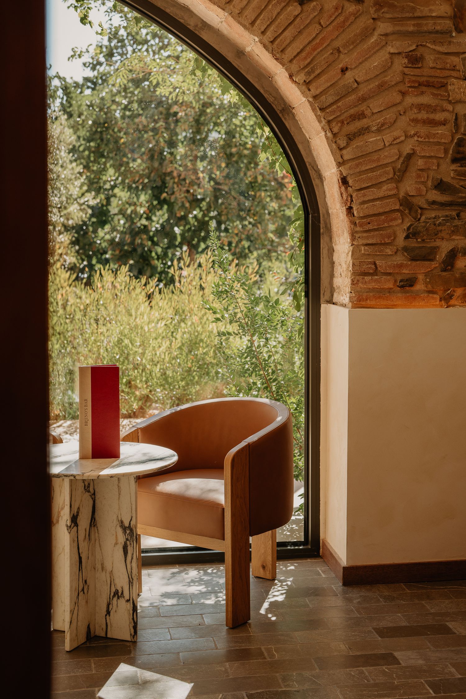 Curved archway frames a modern seating area with tan chairs and white tables in a rustic brick-walled space.