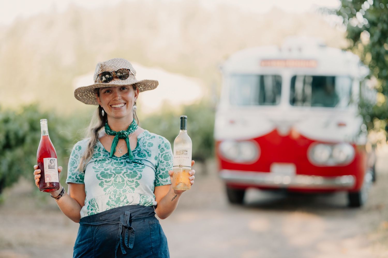 Someone holding bottles of drinks while standing in front of a vintage red and white truck on a sunny day.