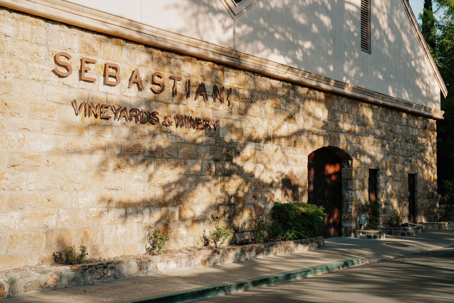 Sebastiani Vineyards and Winery exterior stone building facade with tree shadows at golden hour.