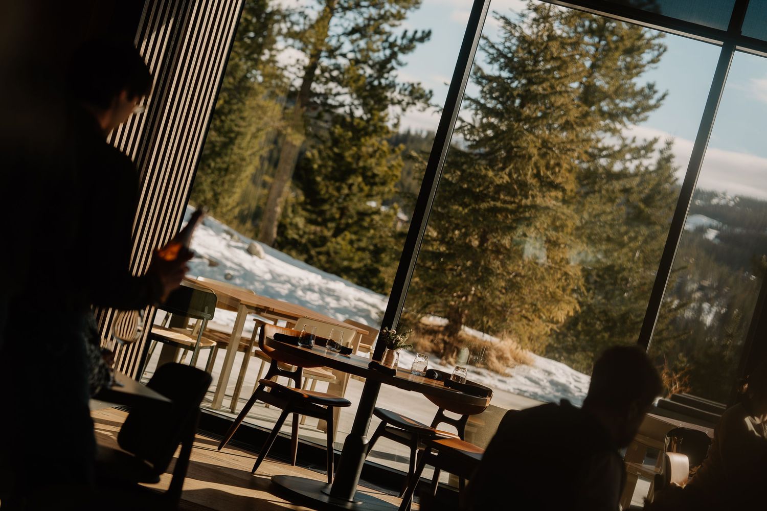 Modern restaurant interior with panoramic windows overlooking snowy mountain landscape.