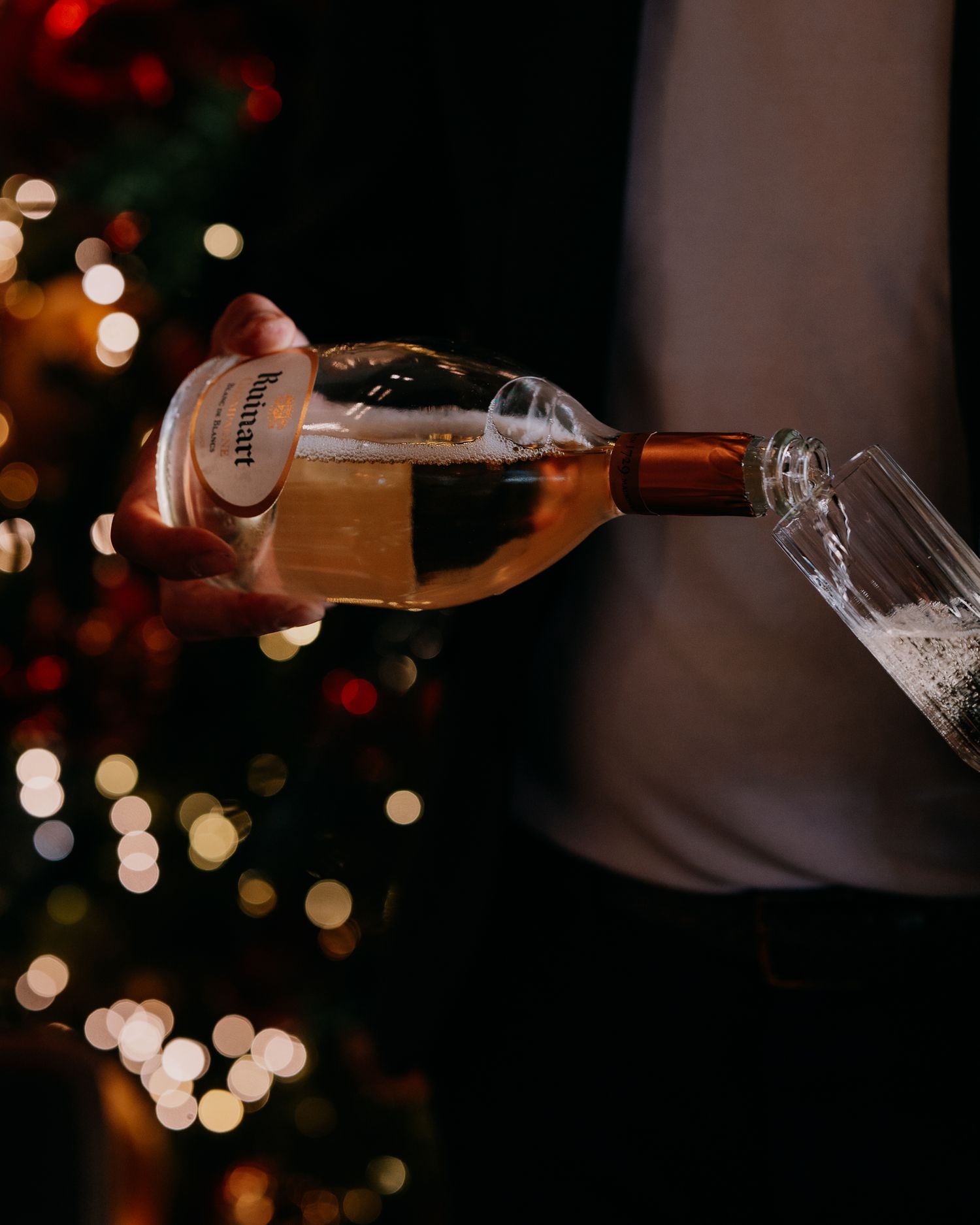 Wine being poured into a glass with blurred Christmas lights bokeh in the background.