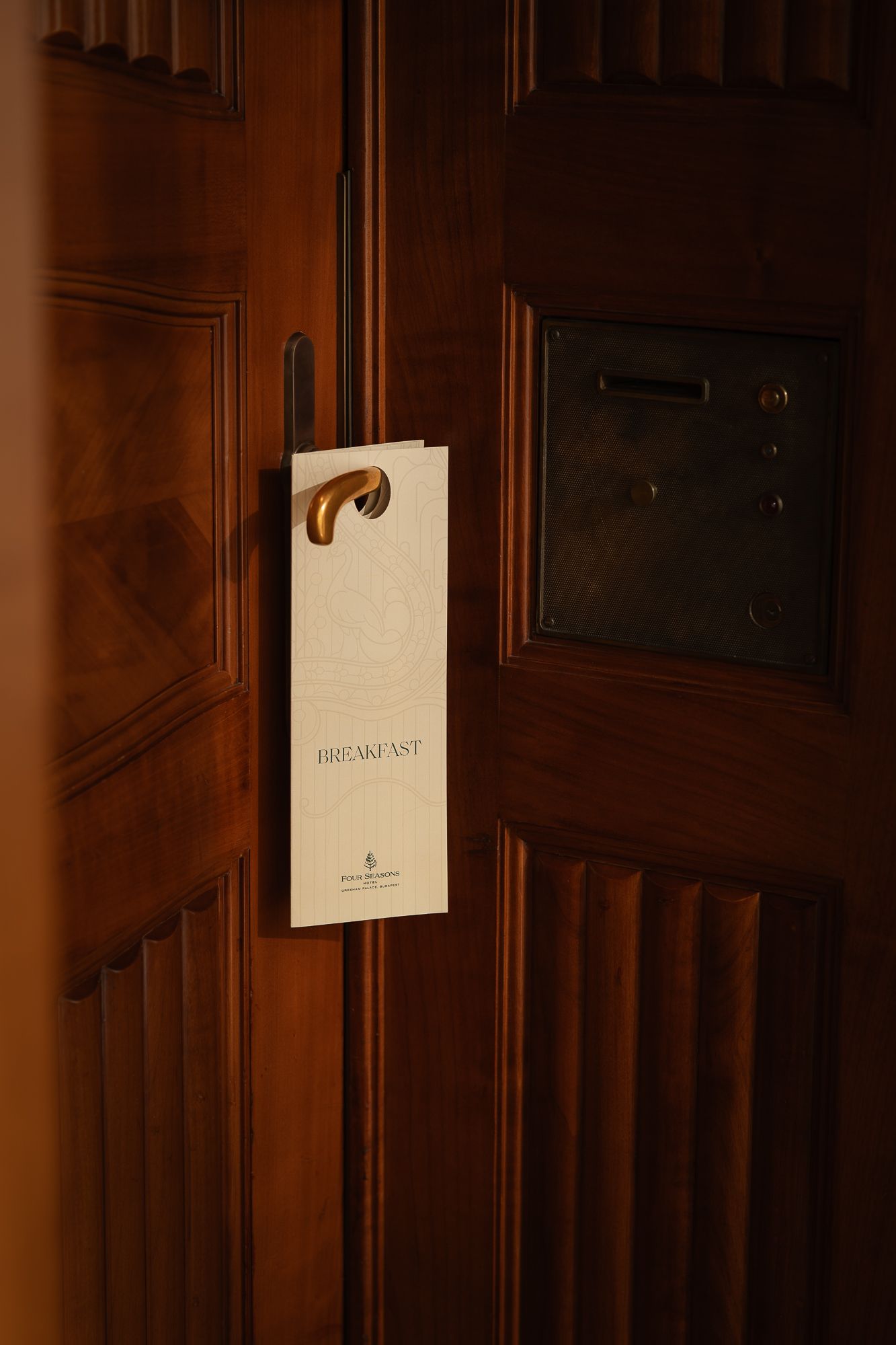 Hotel room door with a breakfast door hanger sign on a dark wooden door with a mail slot.