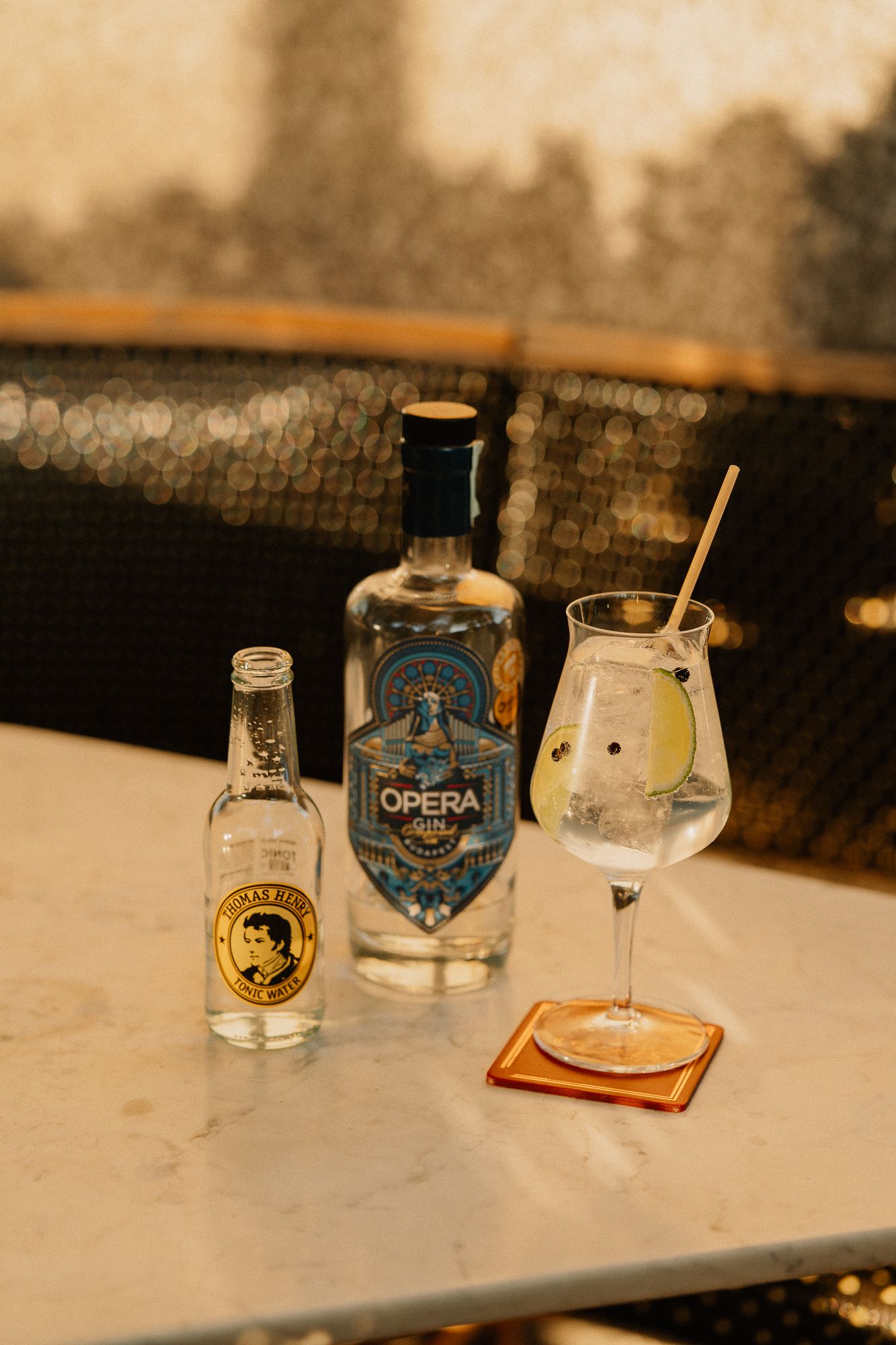 Opera Gin bottle with Thomas Henry tonic water and garnished gin tonic cocktail on marble table.
