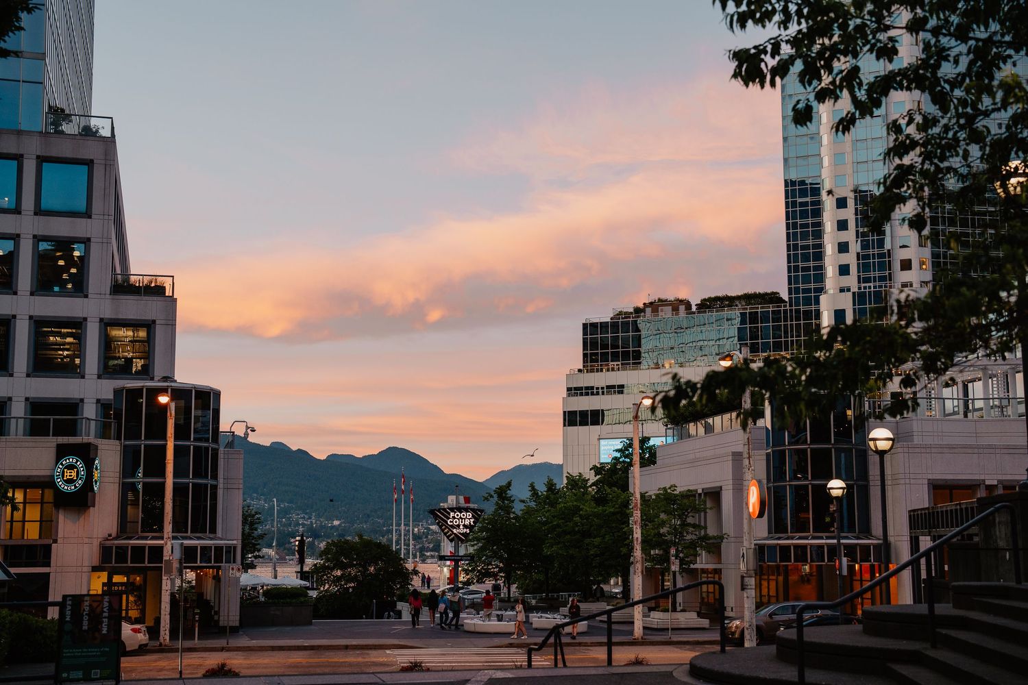 Urban cityscape with modern buildings at sunset against mountain backdrop in Vancouver's downtown core.