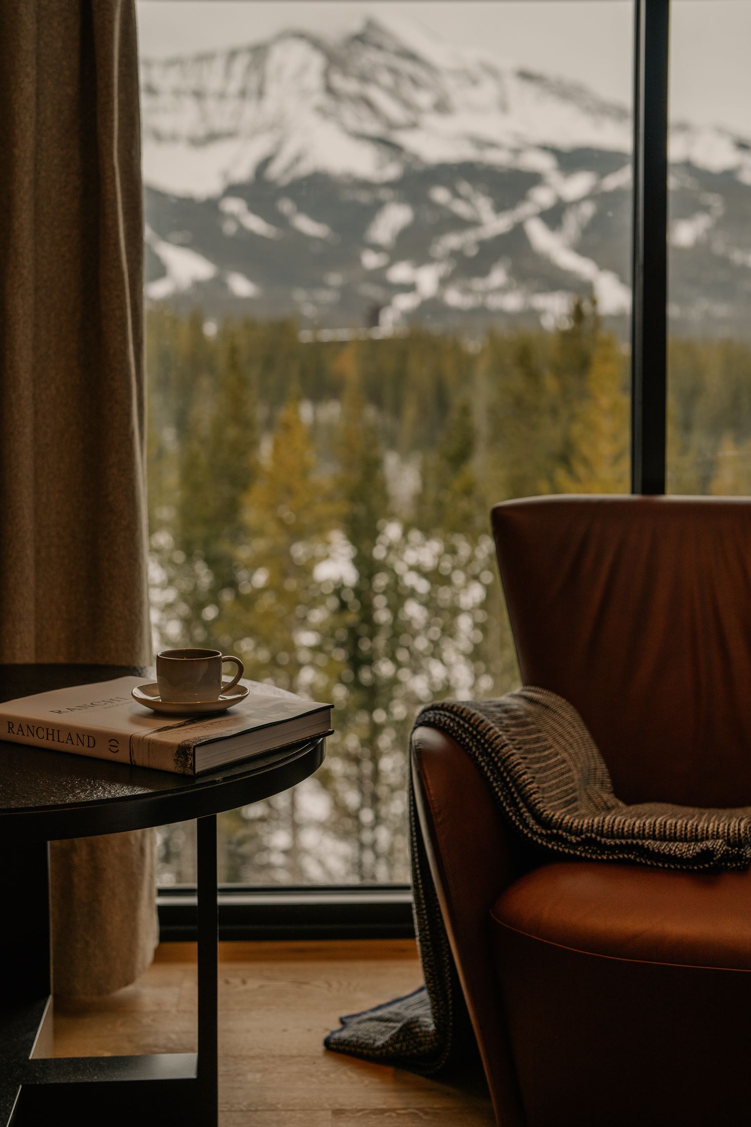 Modern mountain lodge interior with cozy seating and panoramic views of snow-covered peaks.