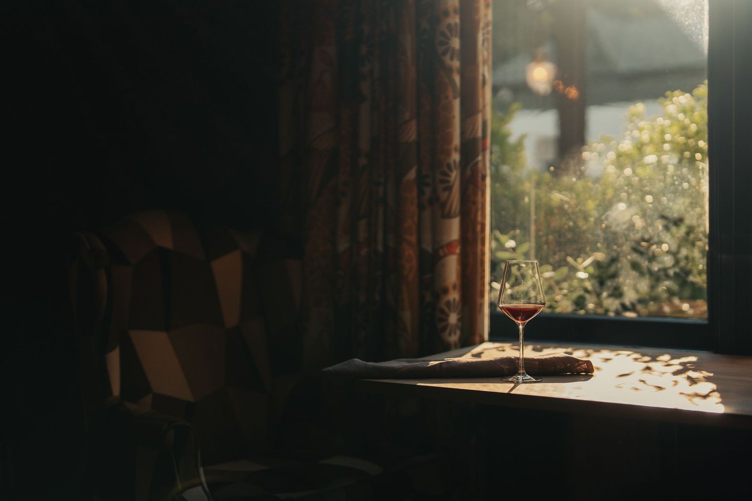 A cat sits in a sunlit window, casting long shadows across the wooden windowsill in a cozy interior setting.