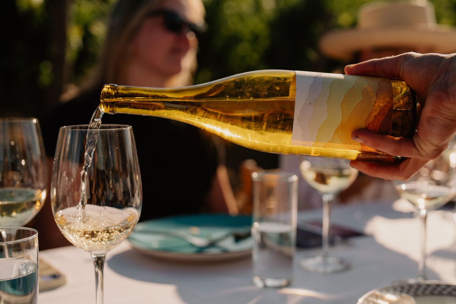 White wine being poured from bottle into wine glass at upscale restaurant setting.