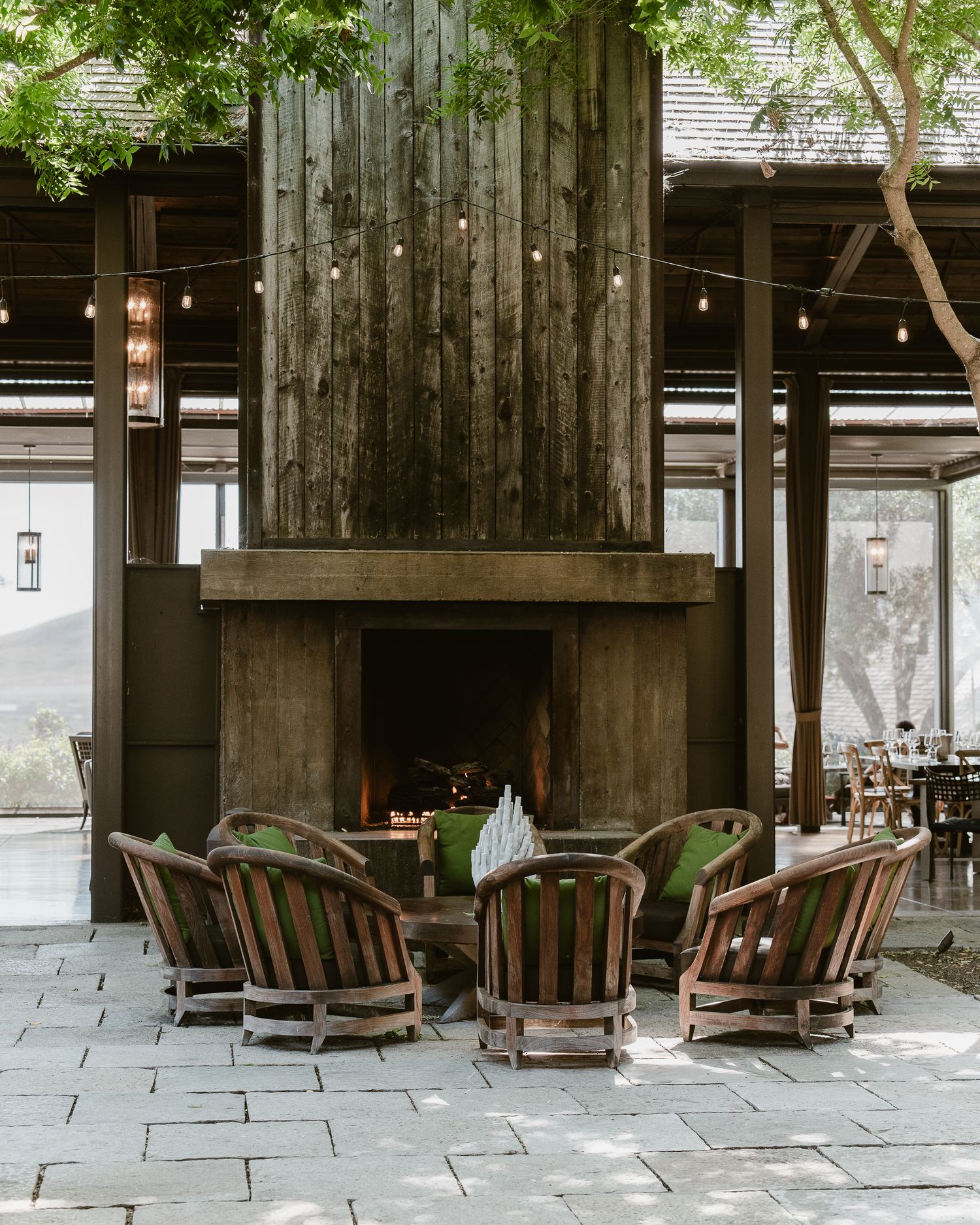 Row of wooden rocking chairs arranged on a rustic covered porch with stone flooring and natural lighting.