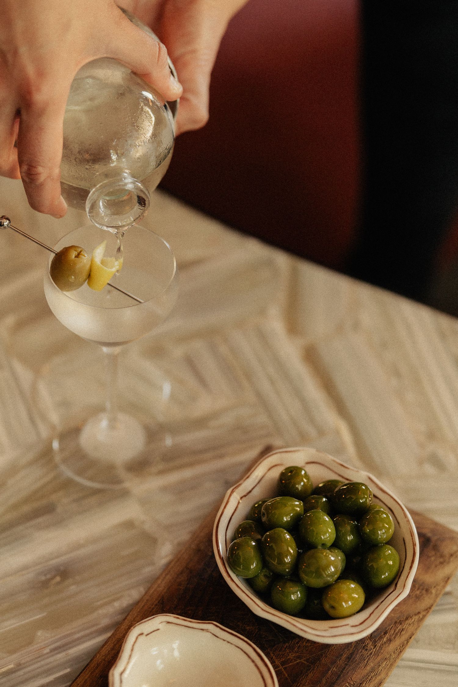 Green olives being served in a small glass bowl on a wooden board with dramatic lighting.