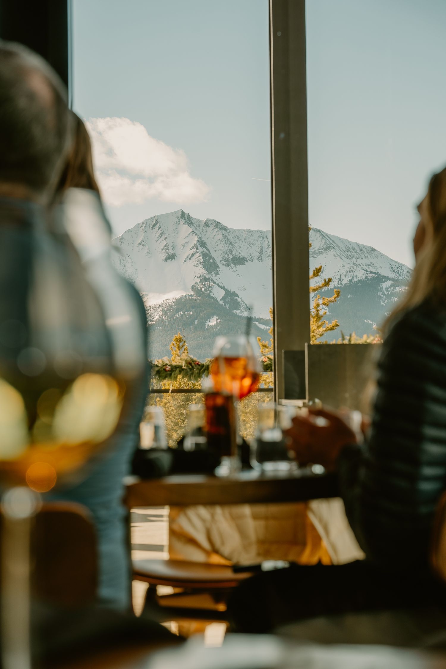 Snow-capped mountain peaks visible through large restaurant windows with drinks in foreground.