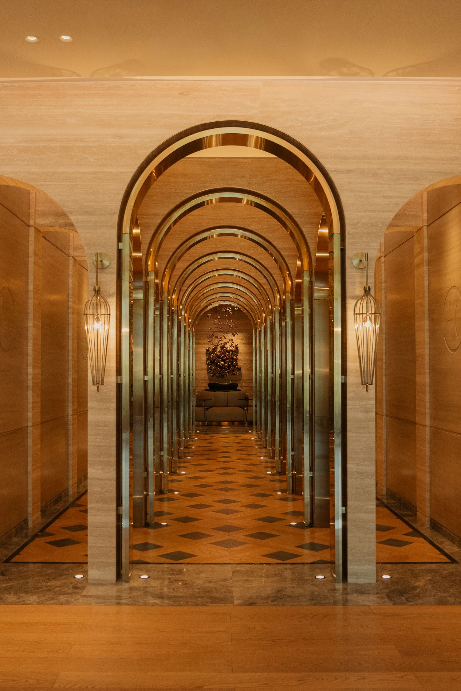 Elegant hotel corridor with repeating golden arches, marble walls, checkered floors, and ornate pendant lights.